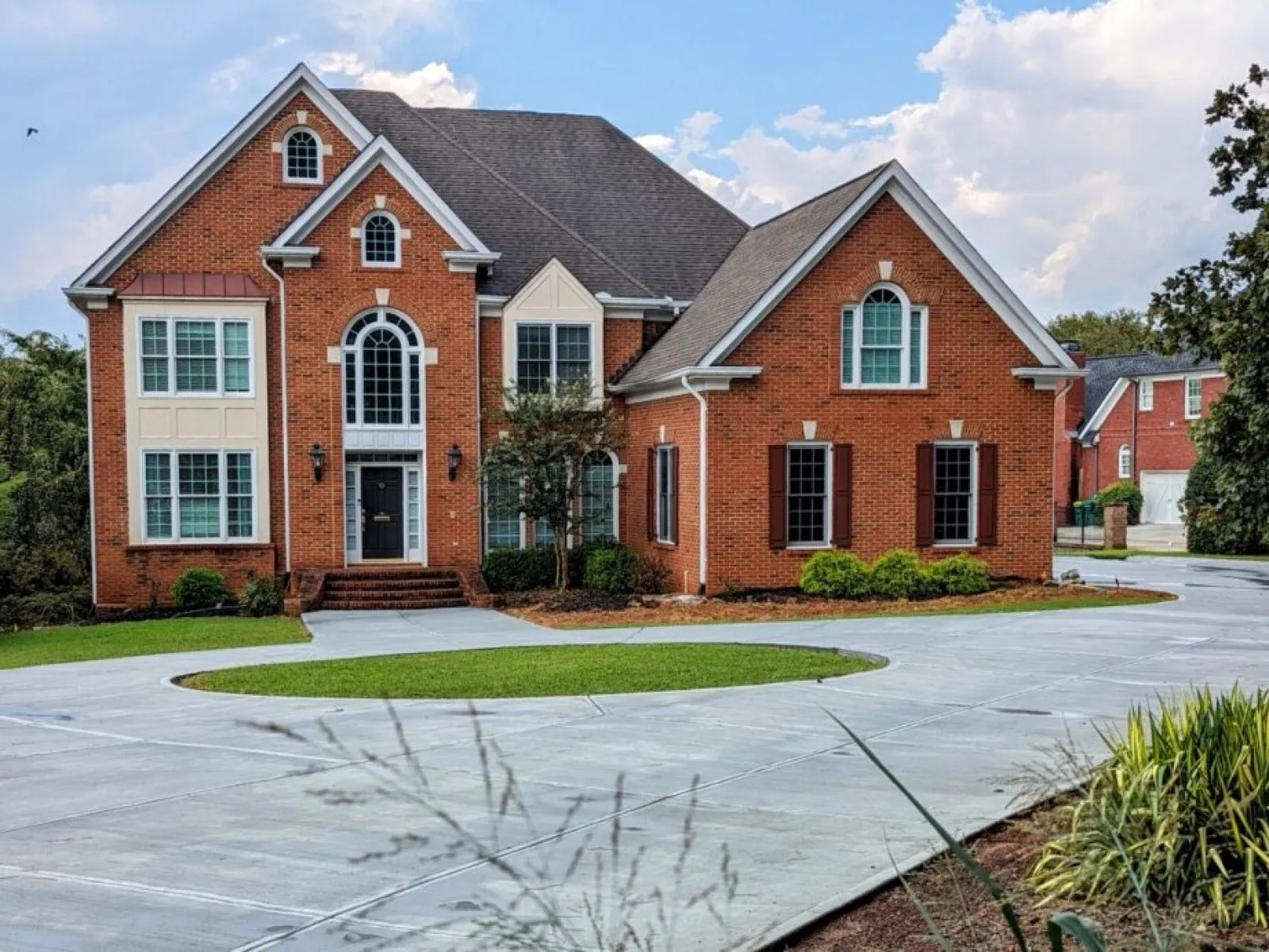 Elegant brick home with large windows and a spacious driveway under a bright sky.