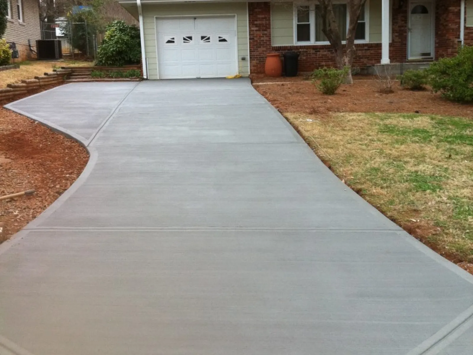 Newly paved concrete driveway leading to a brick house with a garage.