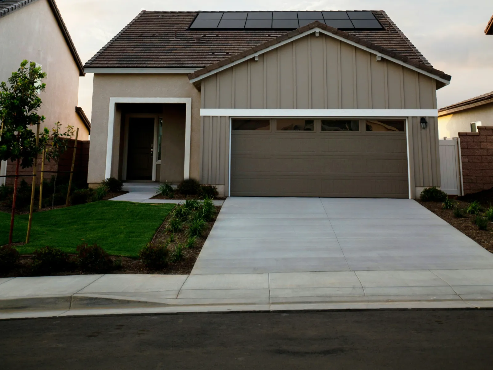 Modern suburban house with solar panels on roof, beige exterior, two-car garage, and a well-maintained front yard.