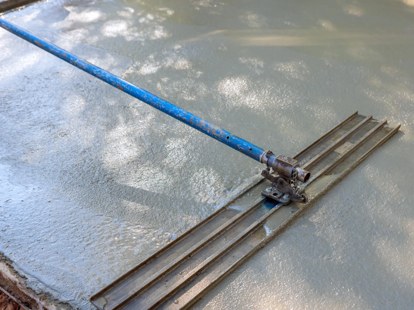 A concrete screed tool smoothing freshly poured cement mix on a construction site.