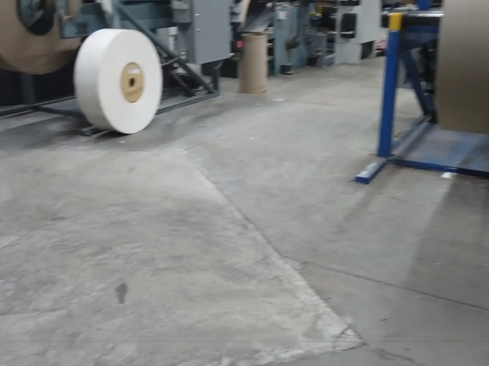 Industrial paper roll machine in a factory with large rolls of paper and metal equipment on a concrete floor.