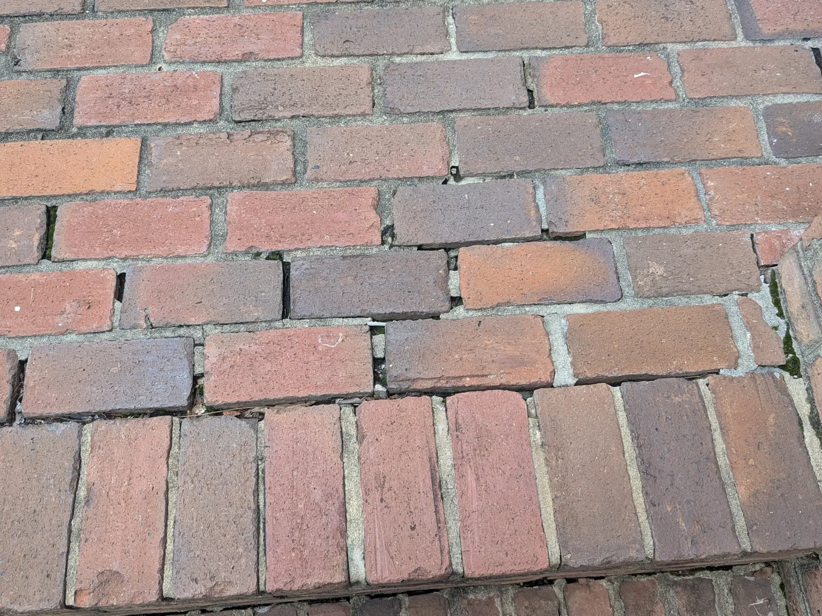 Close-up of uneven red brick pavement with gaps and varying brick alignment outdoors.