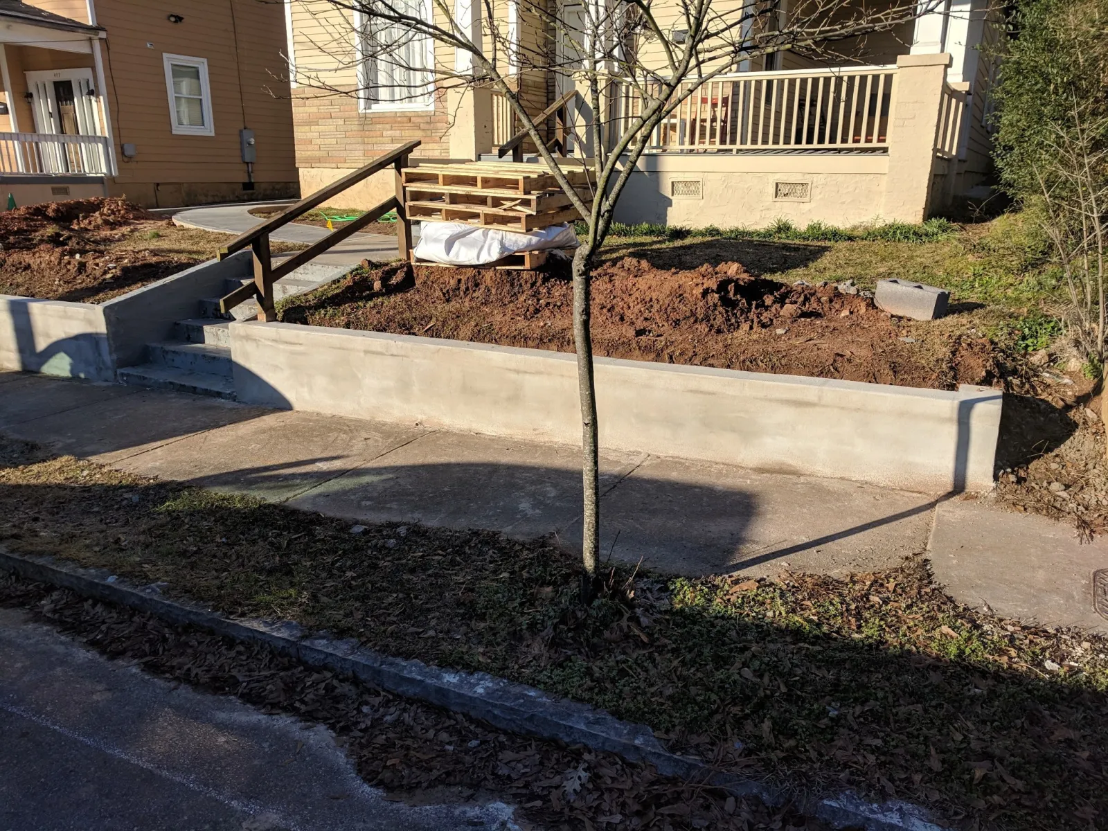 Newly constructed concrete retaining wall and steps in front of a residential house with a small tree.