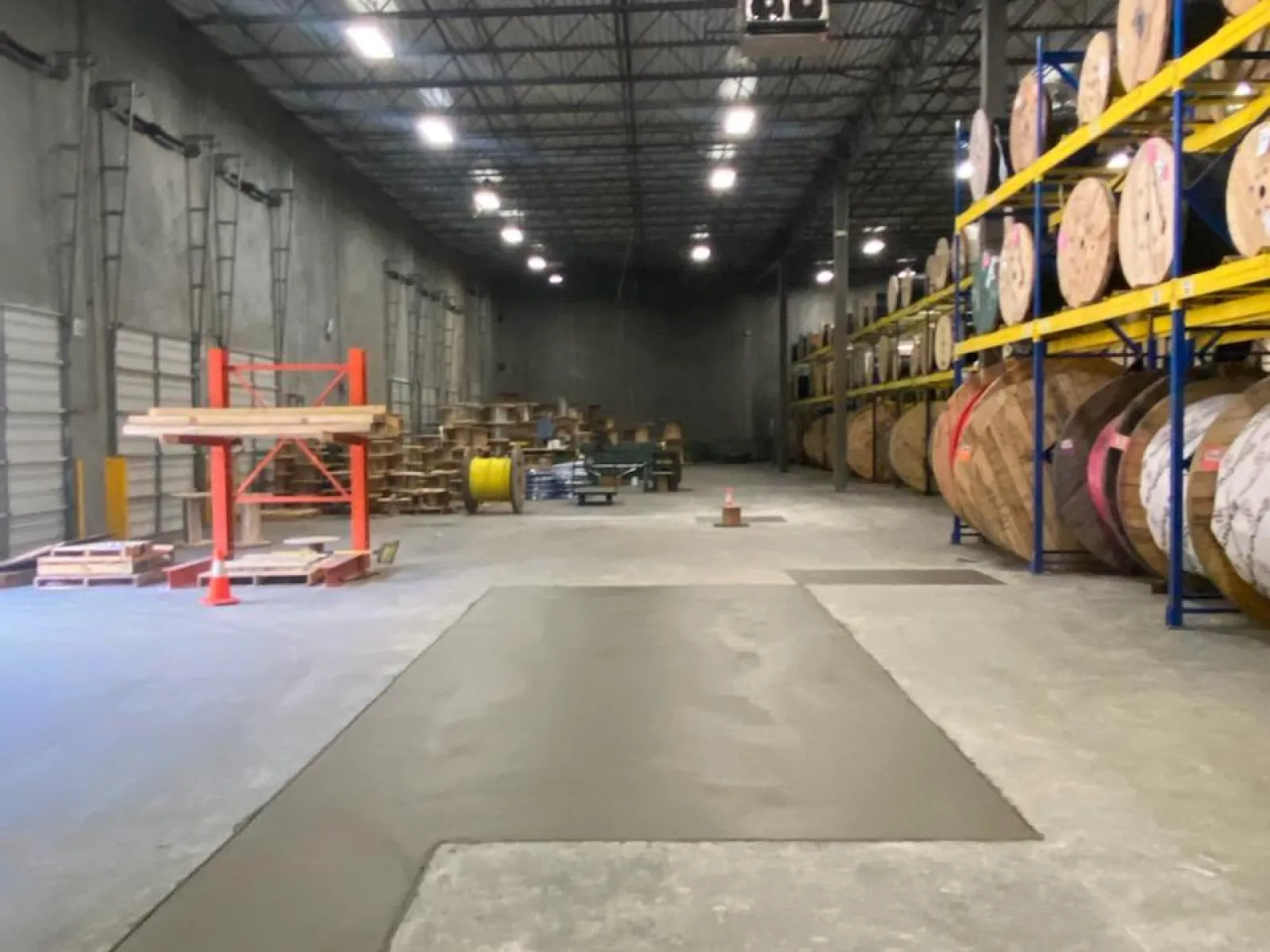 Spacious warehouse interior showcasing large rolls of material and a concrete floor under bright lighting.