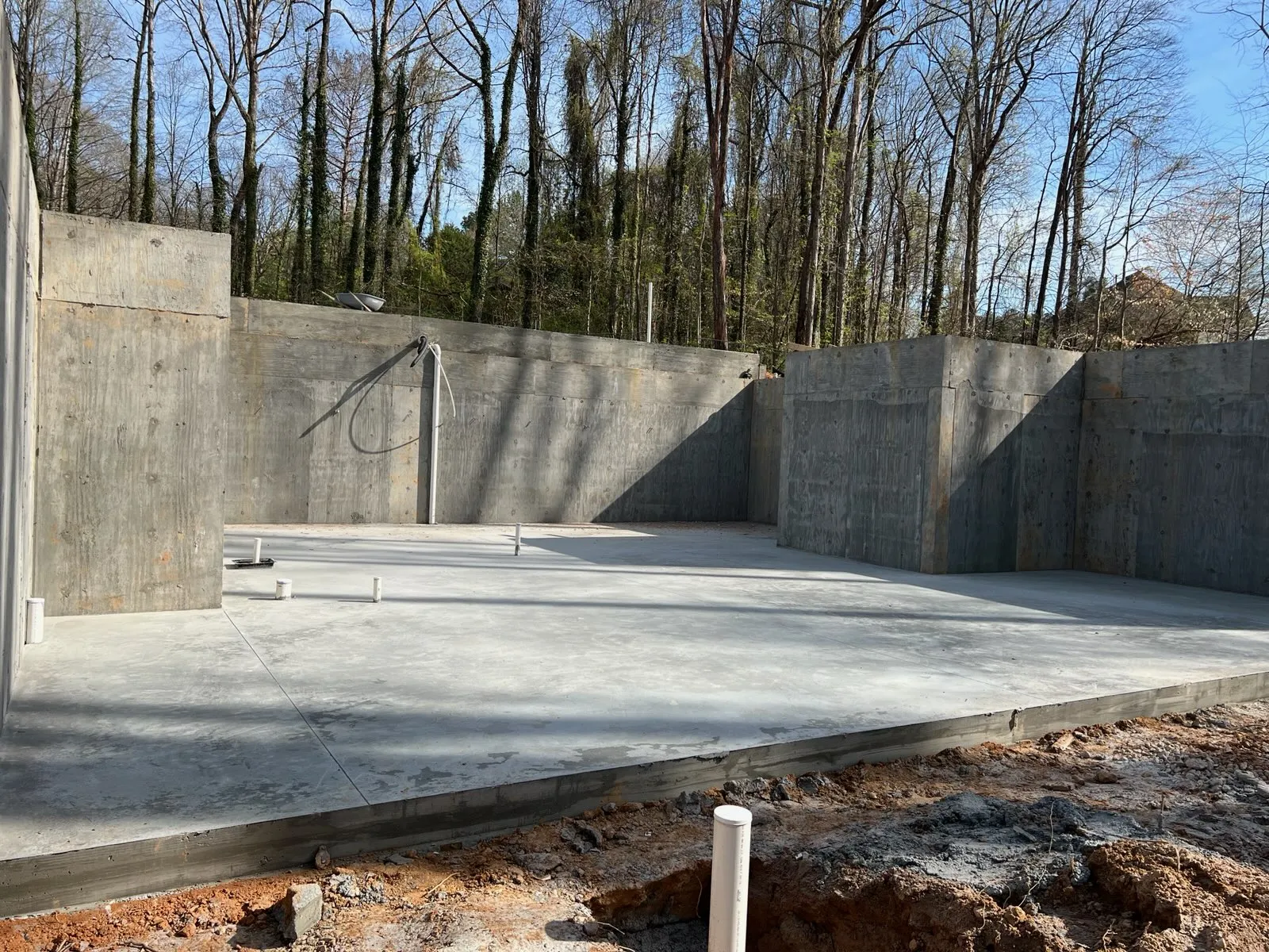 Concrete foundation and basement walls under construction in a wooded outdoor site on a clear day.