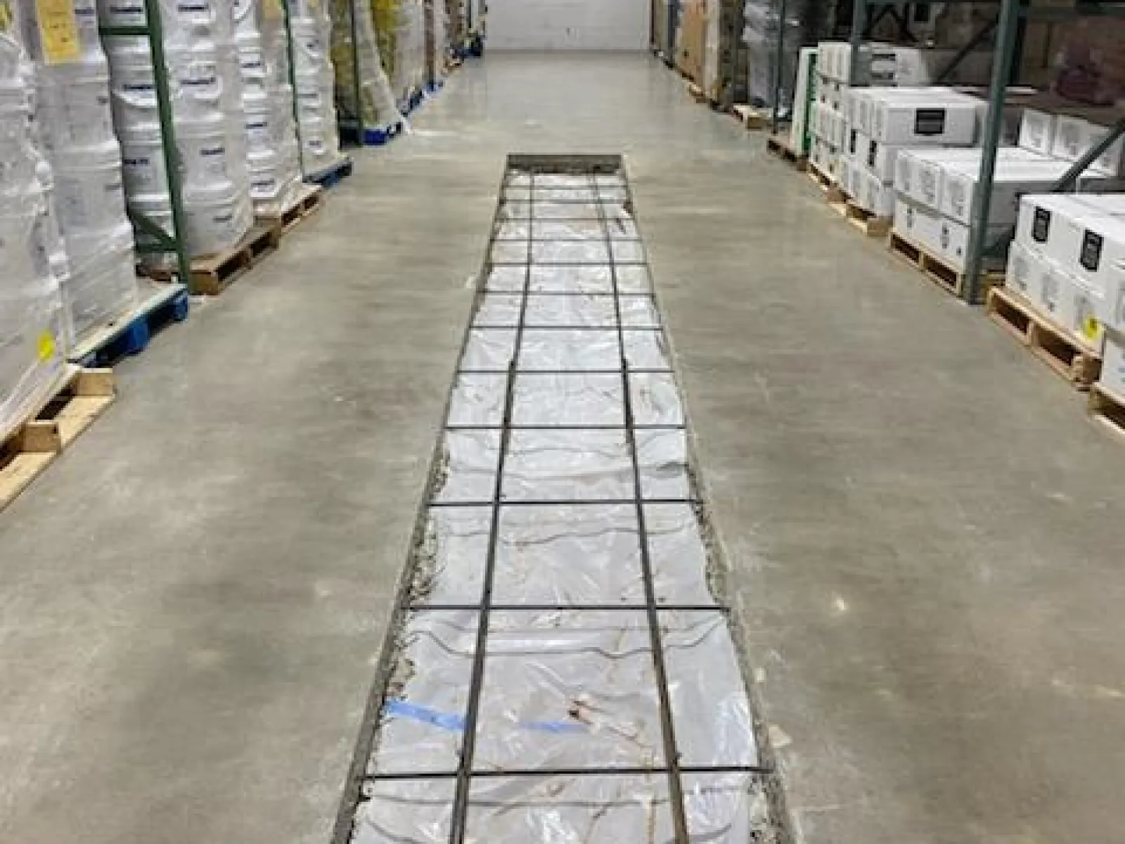 Inside a warehouse displaying a concrete floor with a trench, storage pallets on either side.