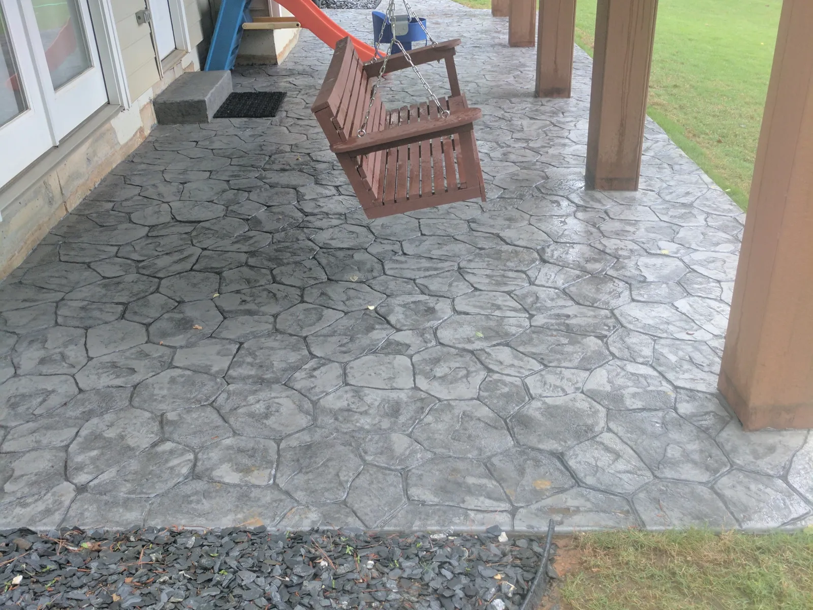 Concrete patio with a stone pattern, featuring a swing and vibrant green lawn.