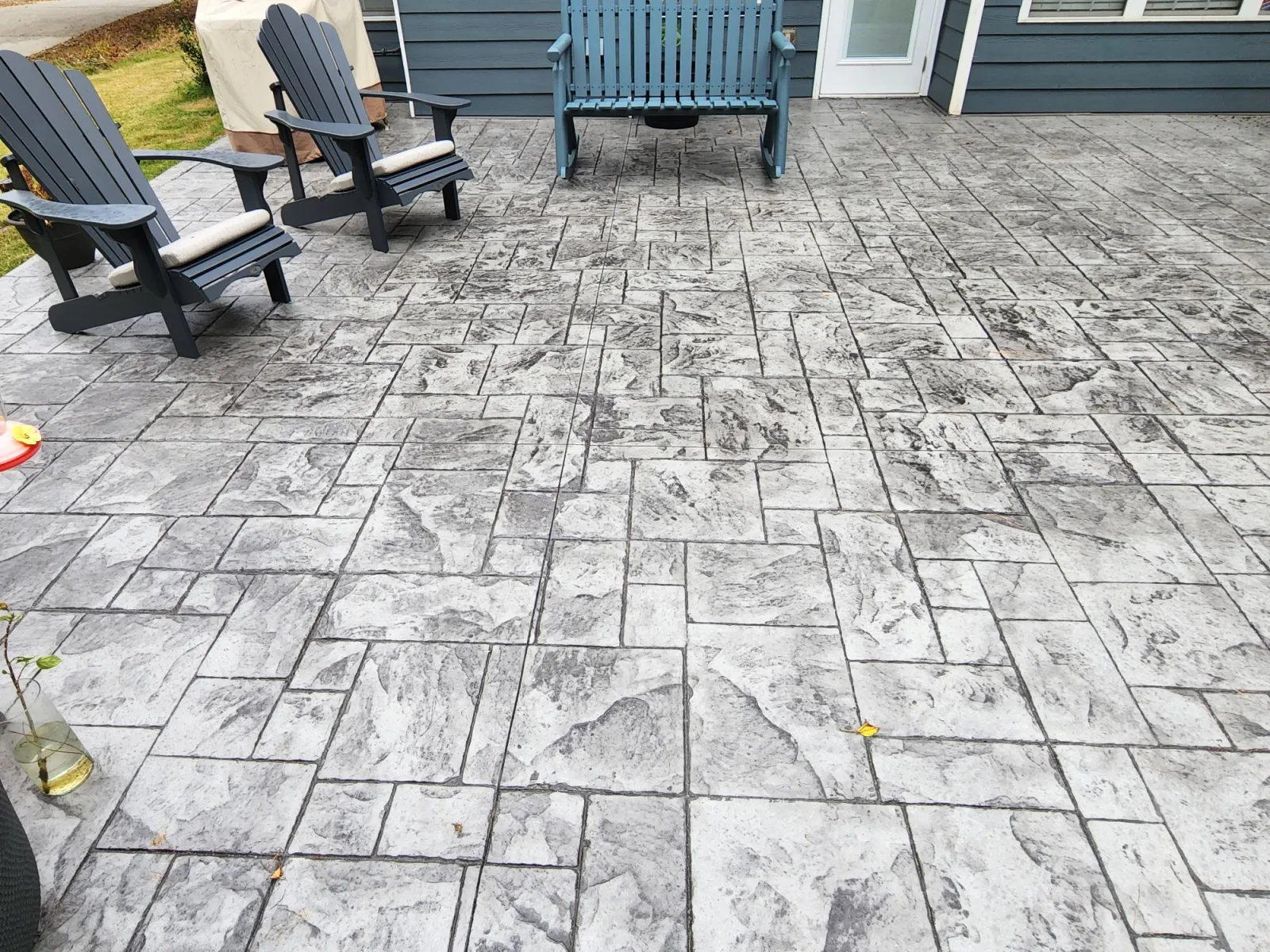 Gray stamped concrete patio with two black adirondack chairs and a cozy outdoor setting.