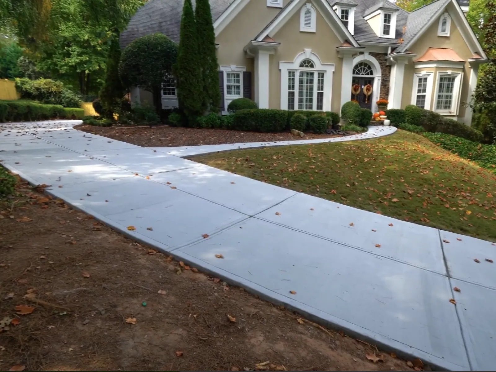 Newly poured concrete driveway and curved walkway leading to a beige house with autumn decorations.