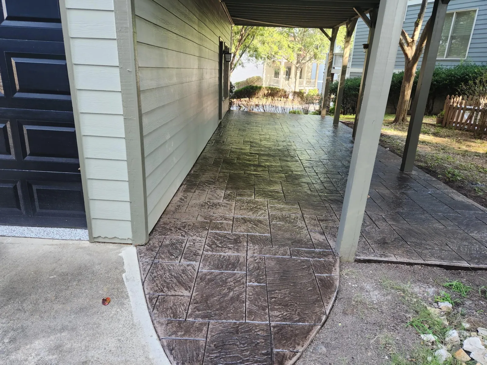 Stylish stamped concrete walkway under a porch leading to a backyard, surrounded by greenery.