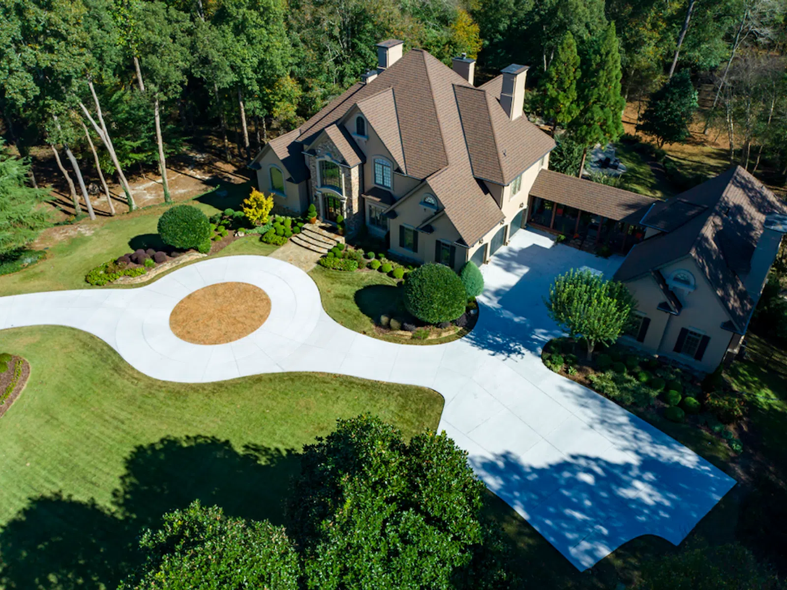 Aerial view of a grand house with a spacious driveway surrounded by lush greenery and a manicured lawn.