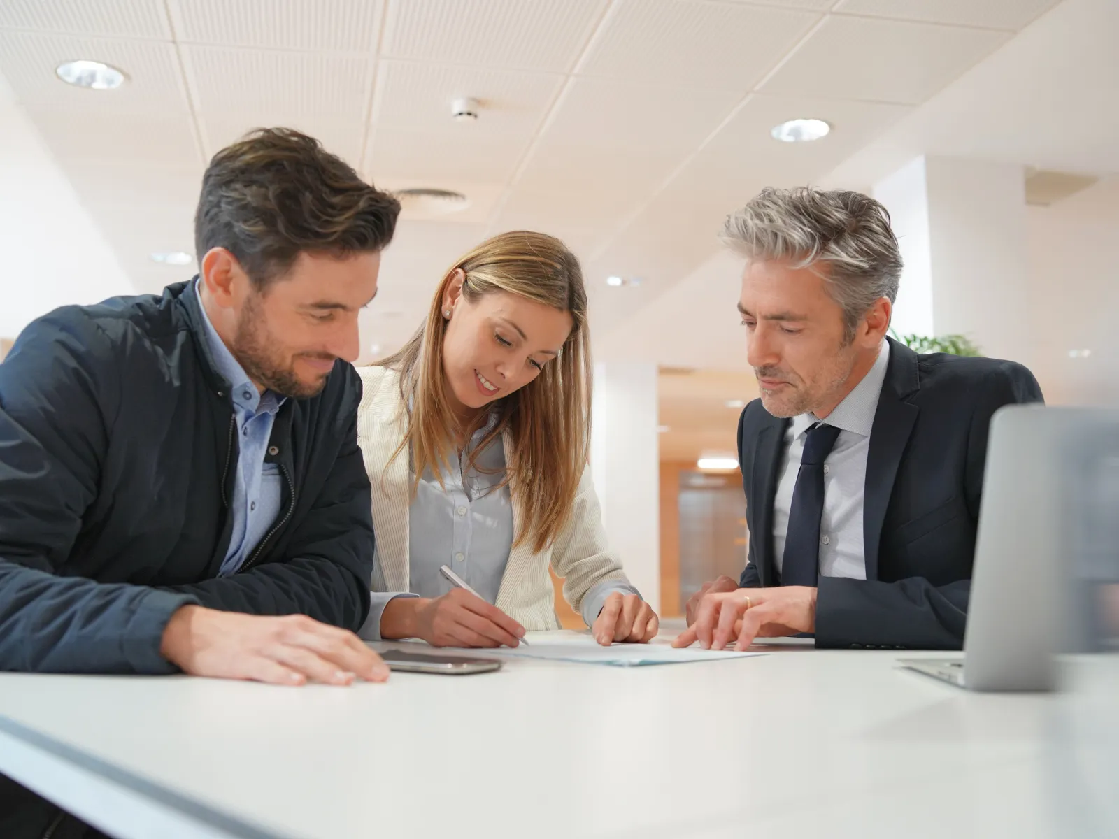 a woman sitting next to two men and signing a contract