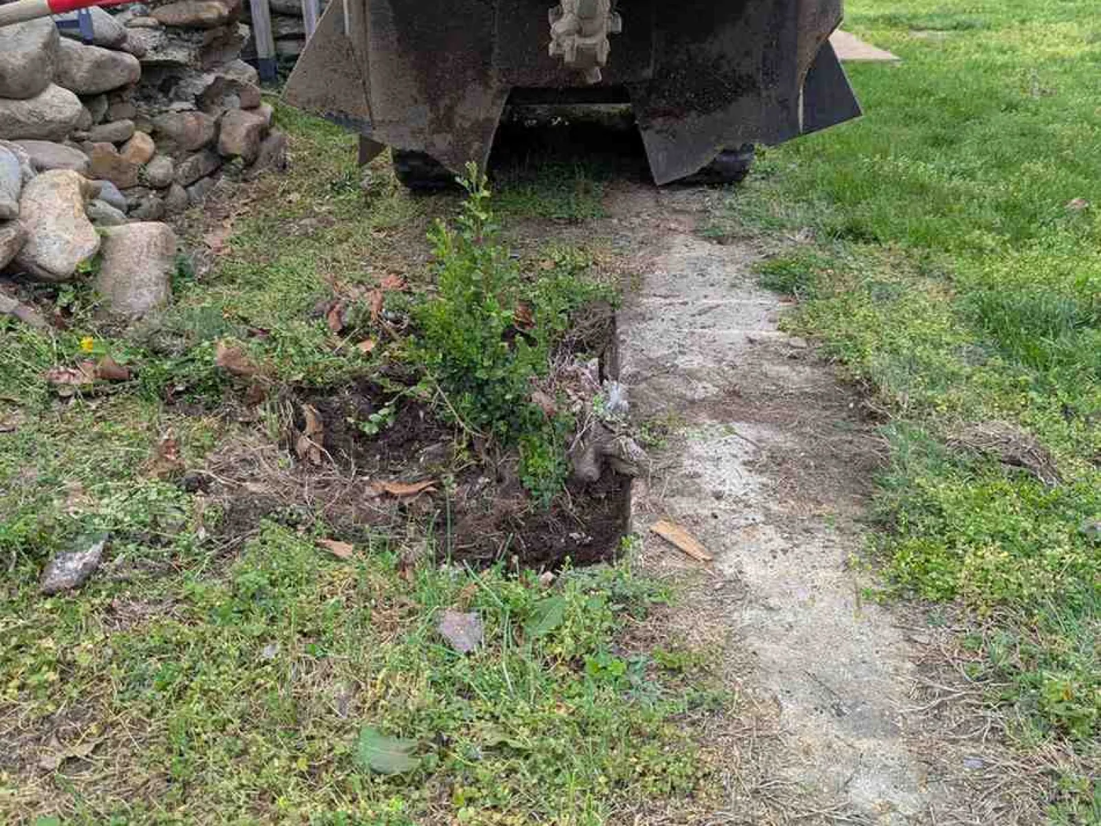 Orange trenching machine digging a narrow trench in green grass near a stone wall and RV.
