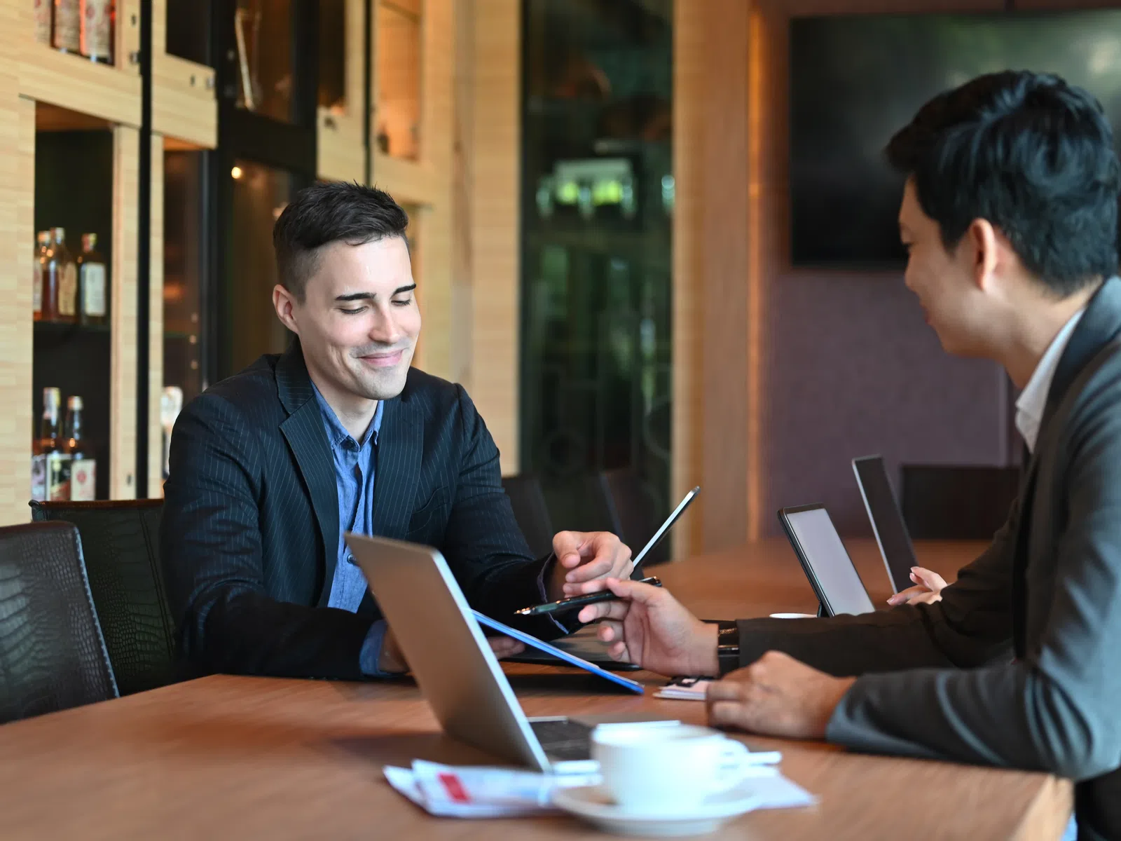 Three professionals in business attire collaborating with laptops and documents in a modern office setting.