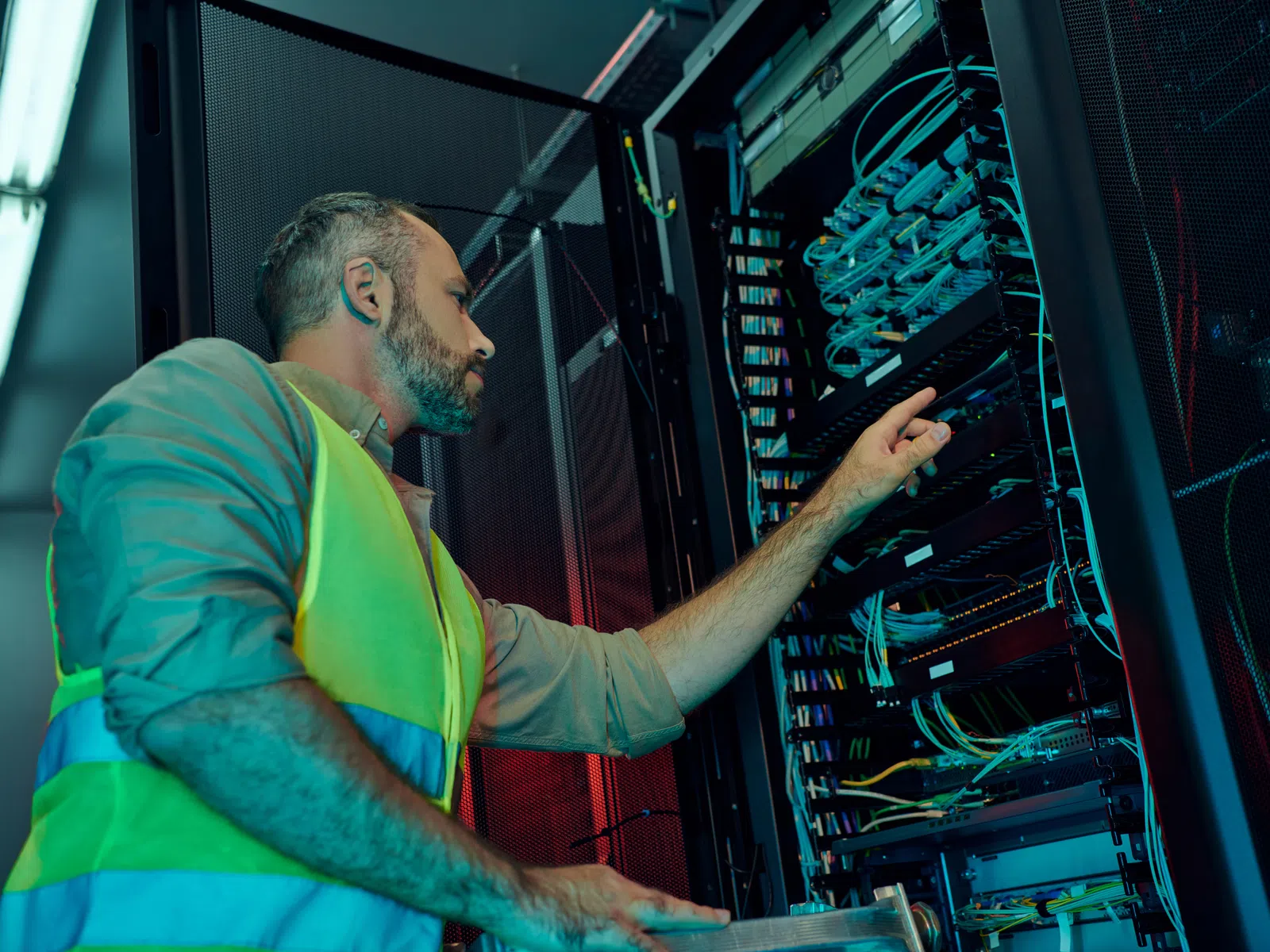 Technician in a reflective vest working on server hardware in a data center rack with network cables.