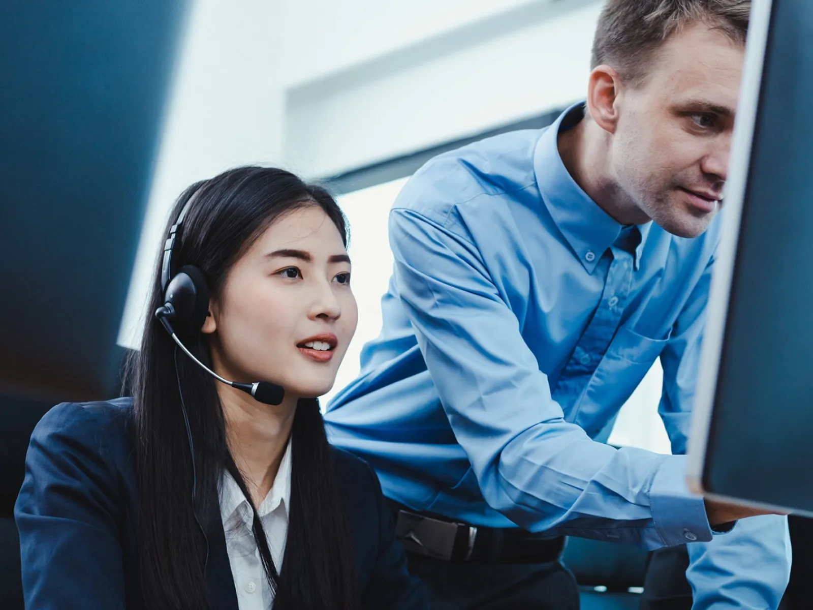 Businesswoman with headset working on computer while male colleague assists in modern office setting
