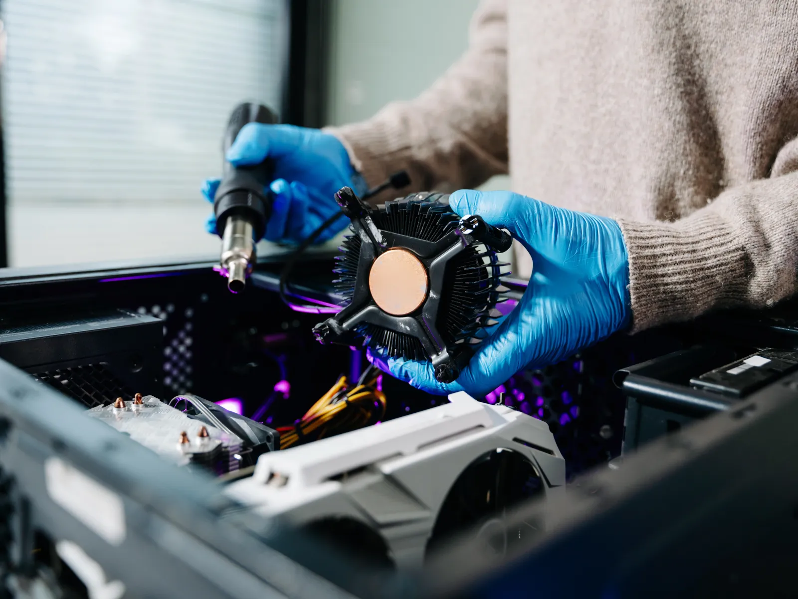 Technician with blue gloves installing a CPU cooler inside an open desktop computer case.