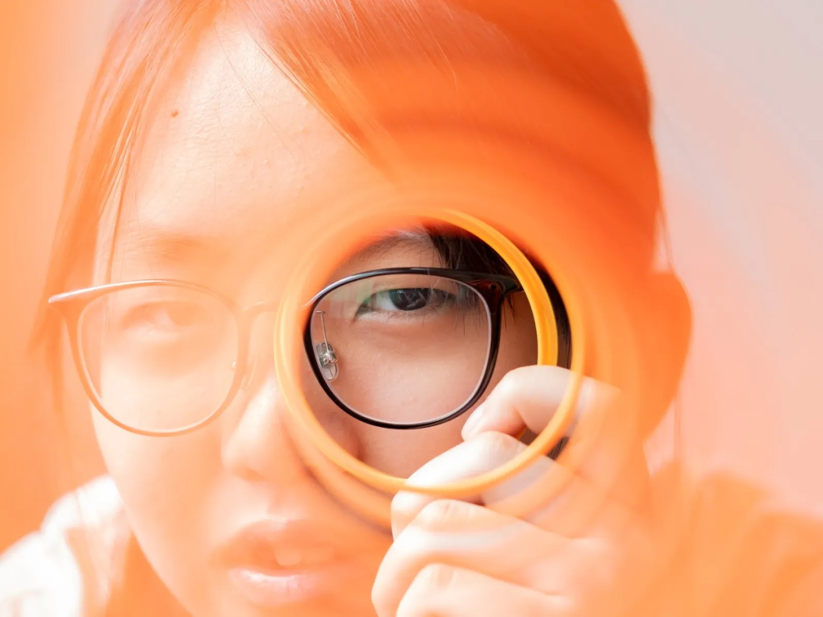 Person with glasses looking through an orange circular object with orange light overlay.
