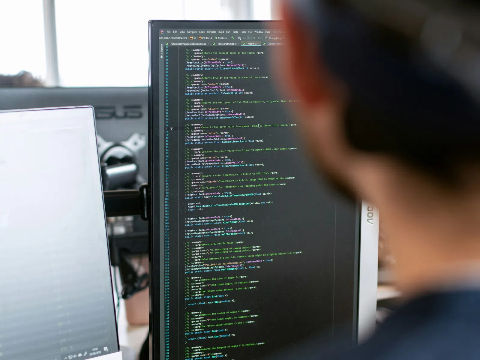 Person viewing computer screen displaying code editor with programming code in an office setting.