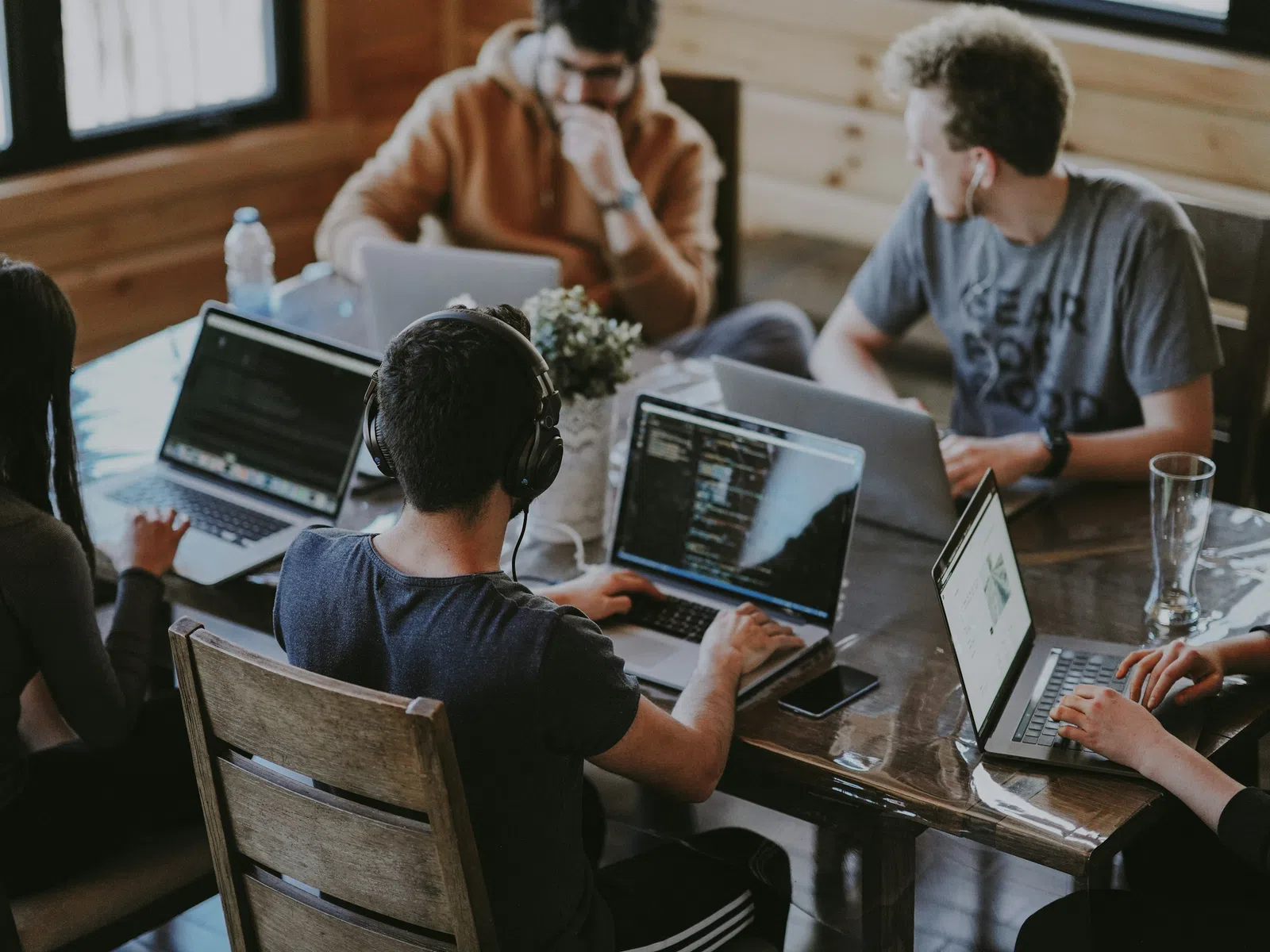 Group of young professionals collaborating on laptops around a wooden table in a cozy workspace.