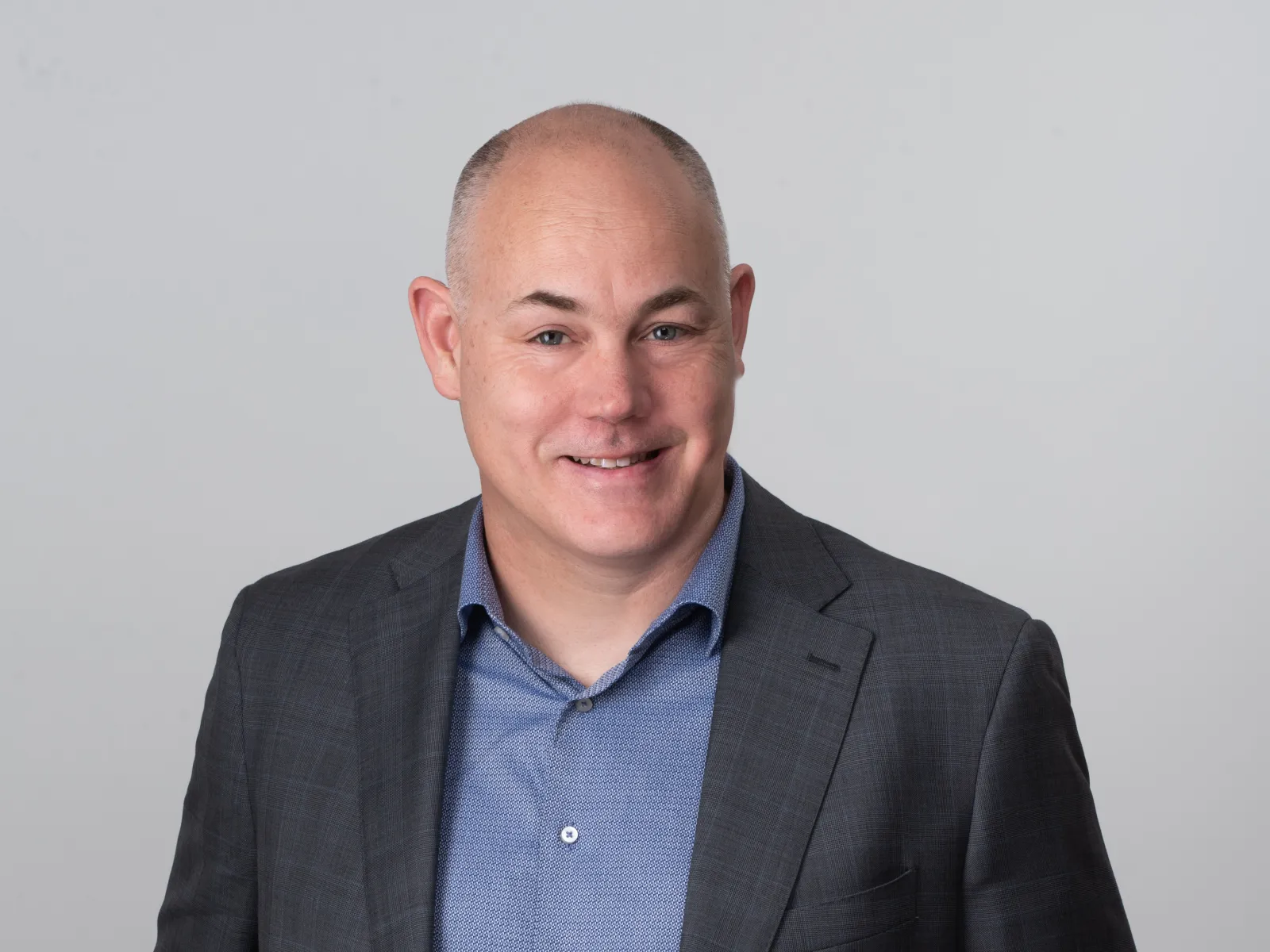 Professional portrait of a man in a suit, smiling against a neutral background.