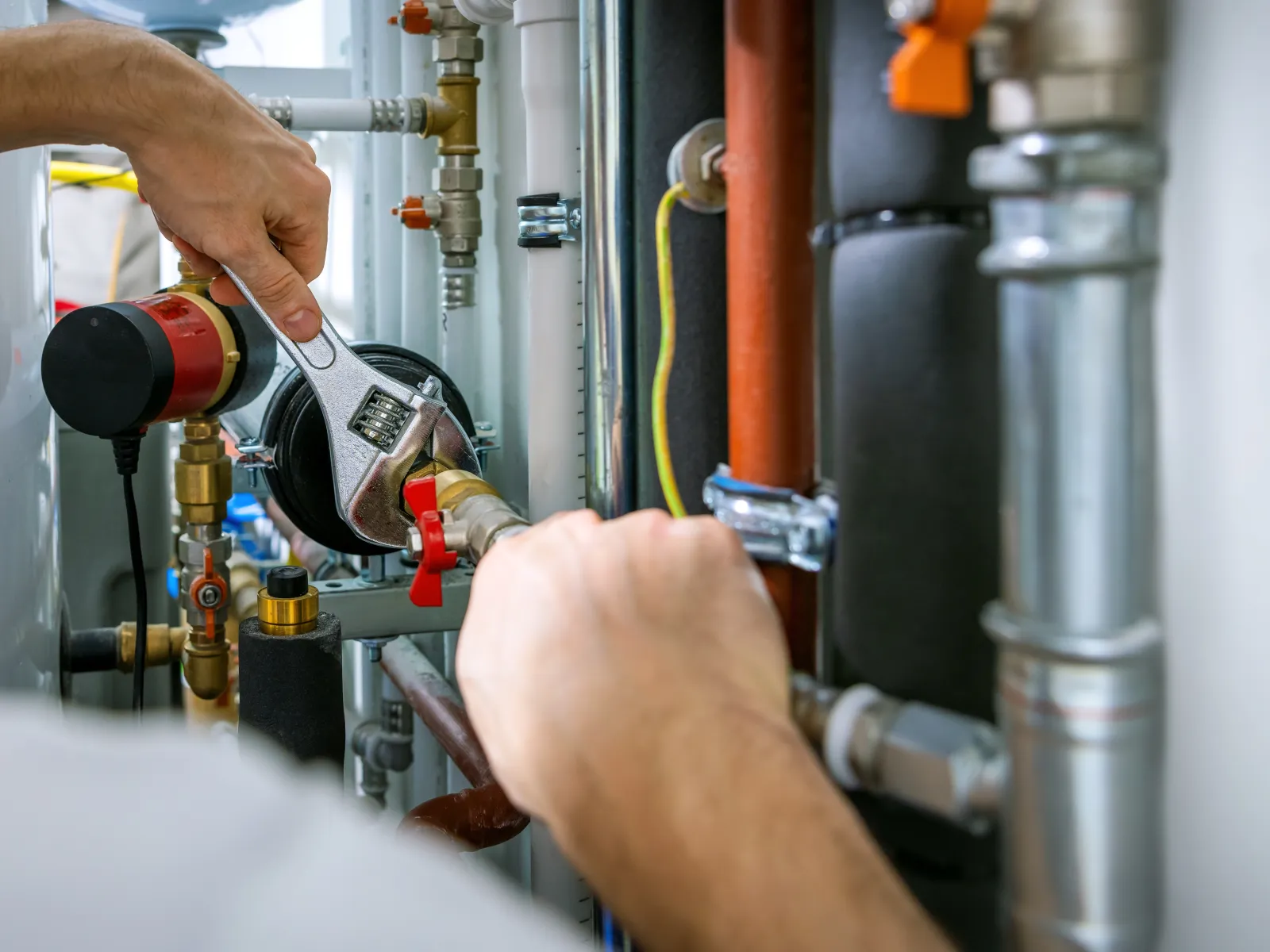 Plumber adjusting pipes and valves with a wrench in a residential plumbing system setup.