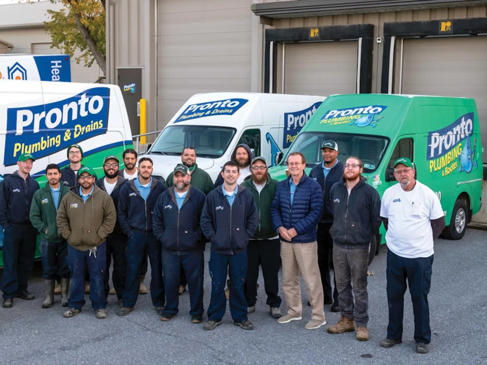 Group of Pronto Plumbing & Drains team members standing in front of company service vans outside a building.