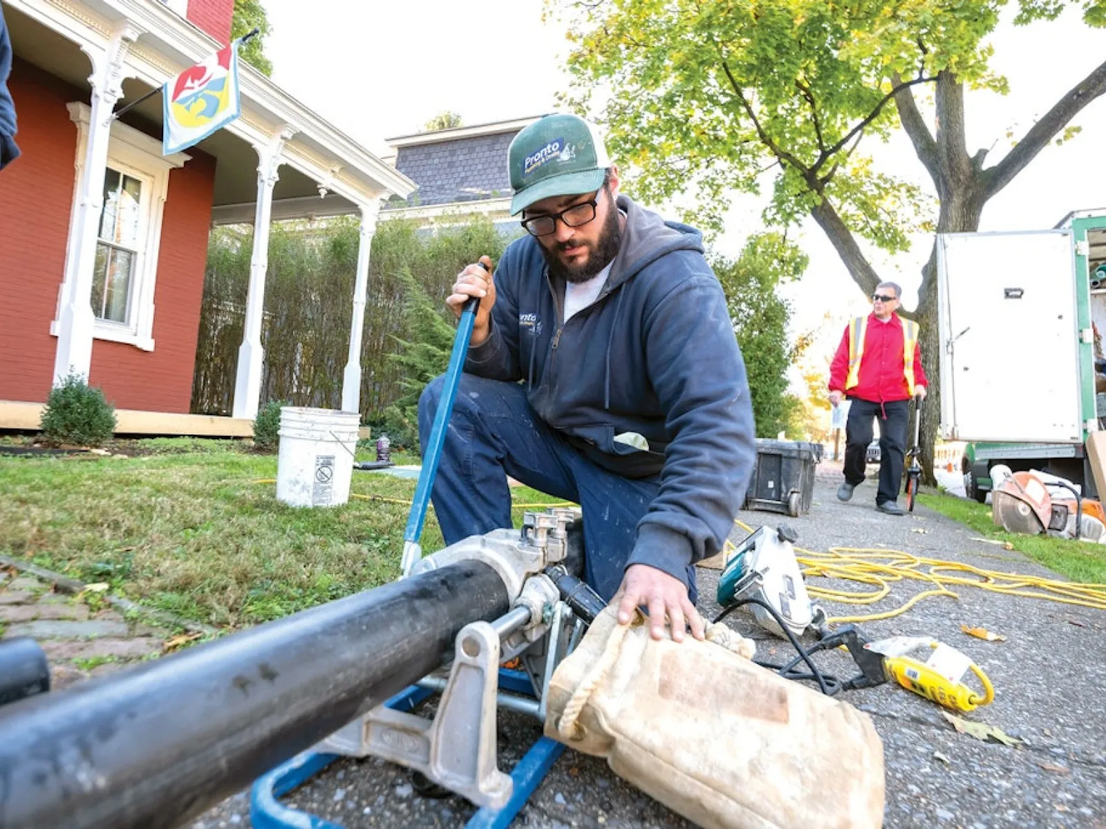 Plumber in checkered shirt fixing bathroom sink plumbing with wrench under white ceramic sink.