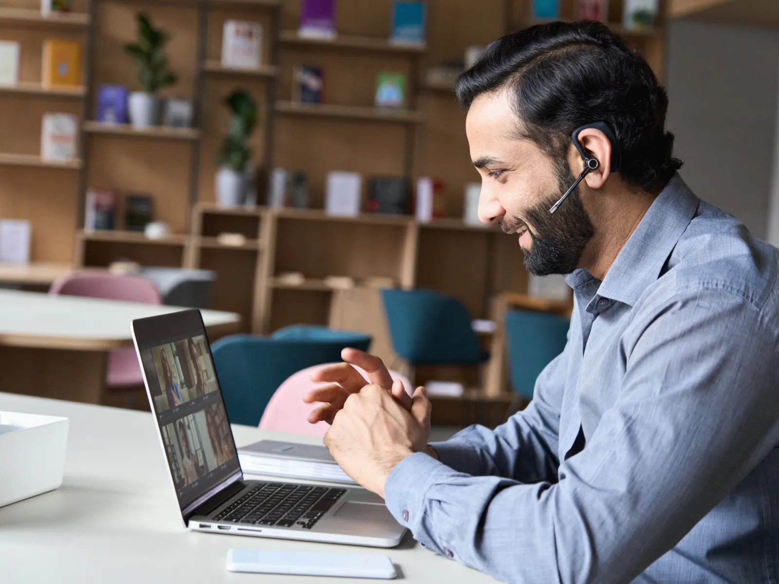 Man with headset smiling and participating in a video conference using a laptop in a modern office.