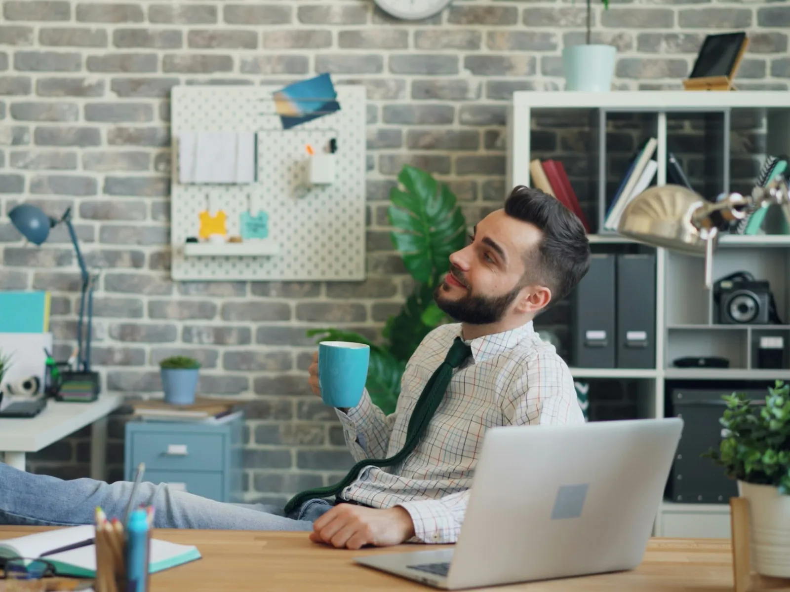 Man in office casual wear relaxing at desk with feet on table holding a coffee mug