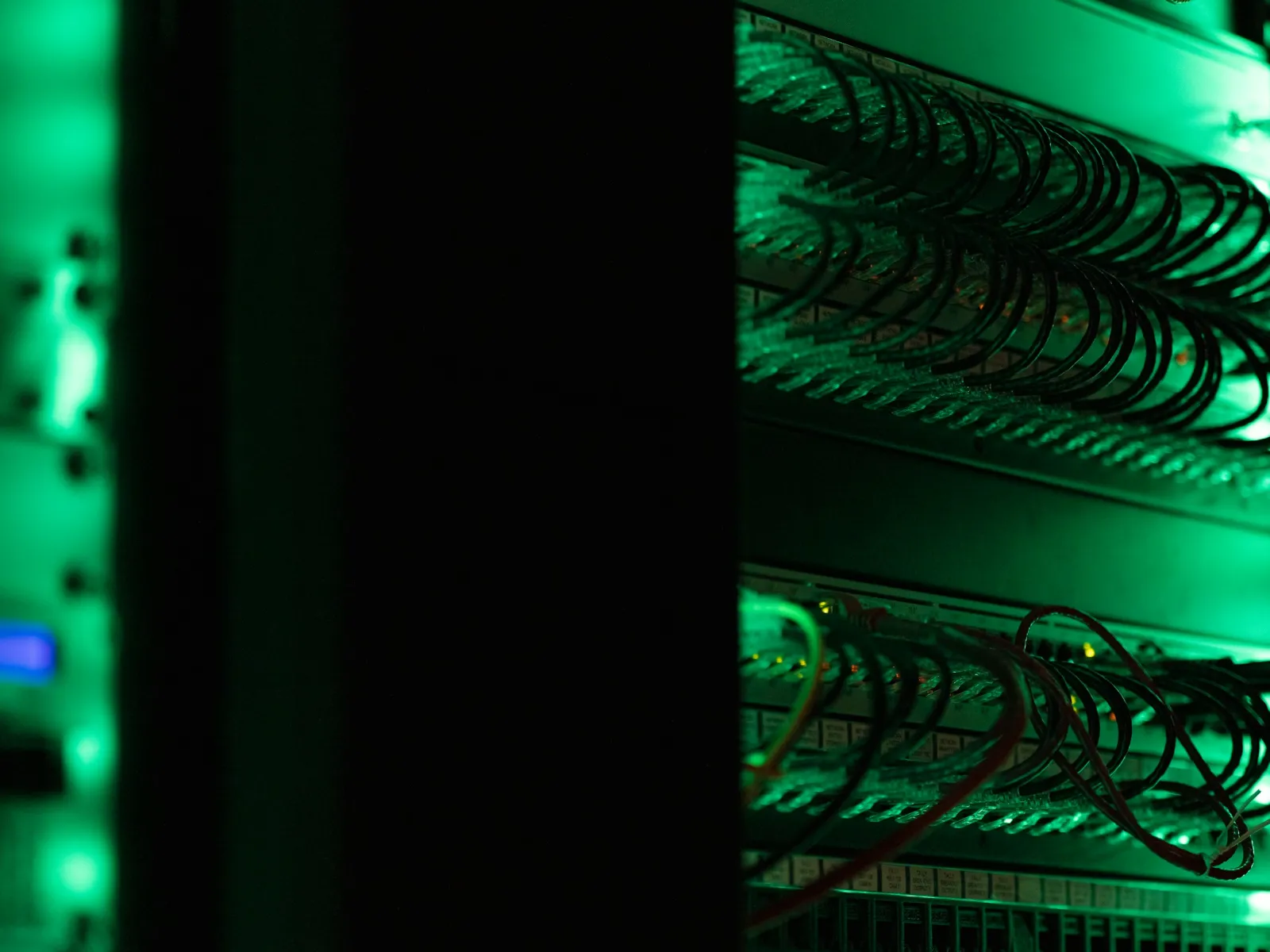 Close-up of green-lit network server racks with cables and patch panels in a dark data center environment