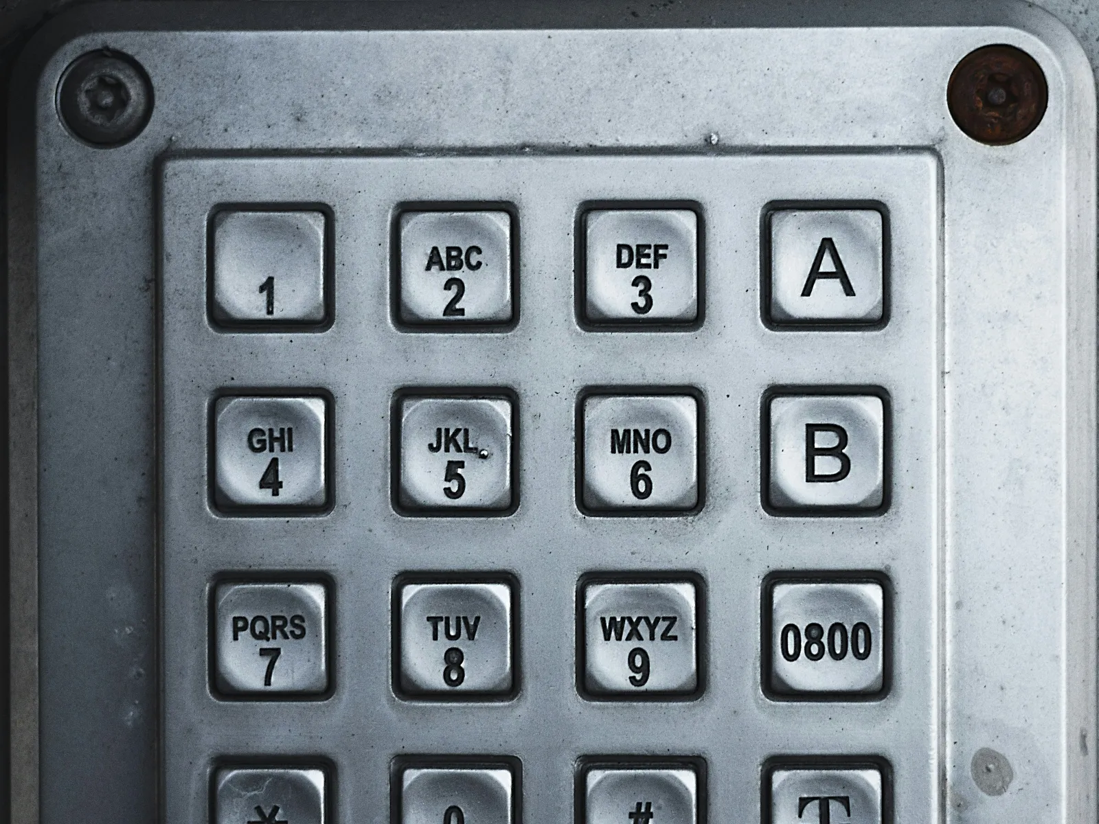 Close-up of a metal keypad with numbers, letters, and symbols on worn buttons in a grid layout.