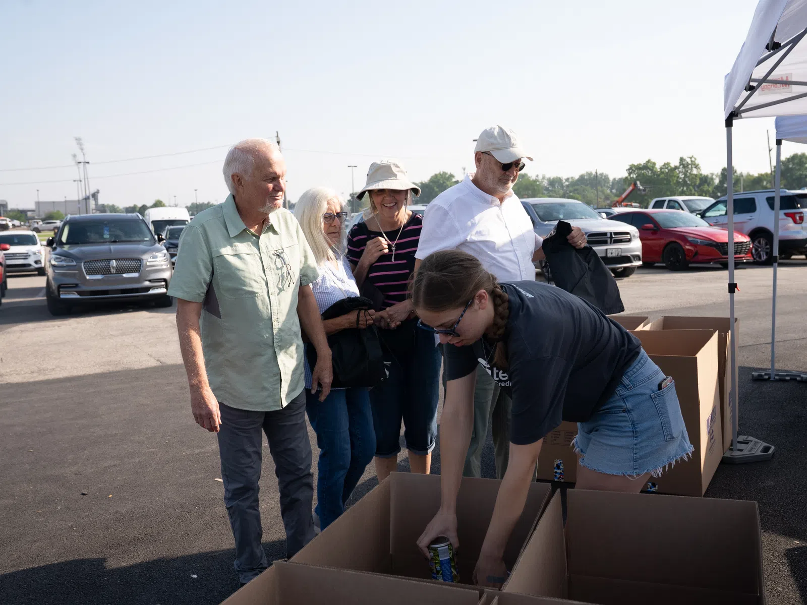 Volunteers and seniors organizing canned goods outdoors in a parking lot donation drive.