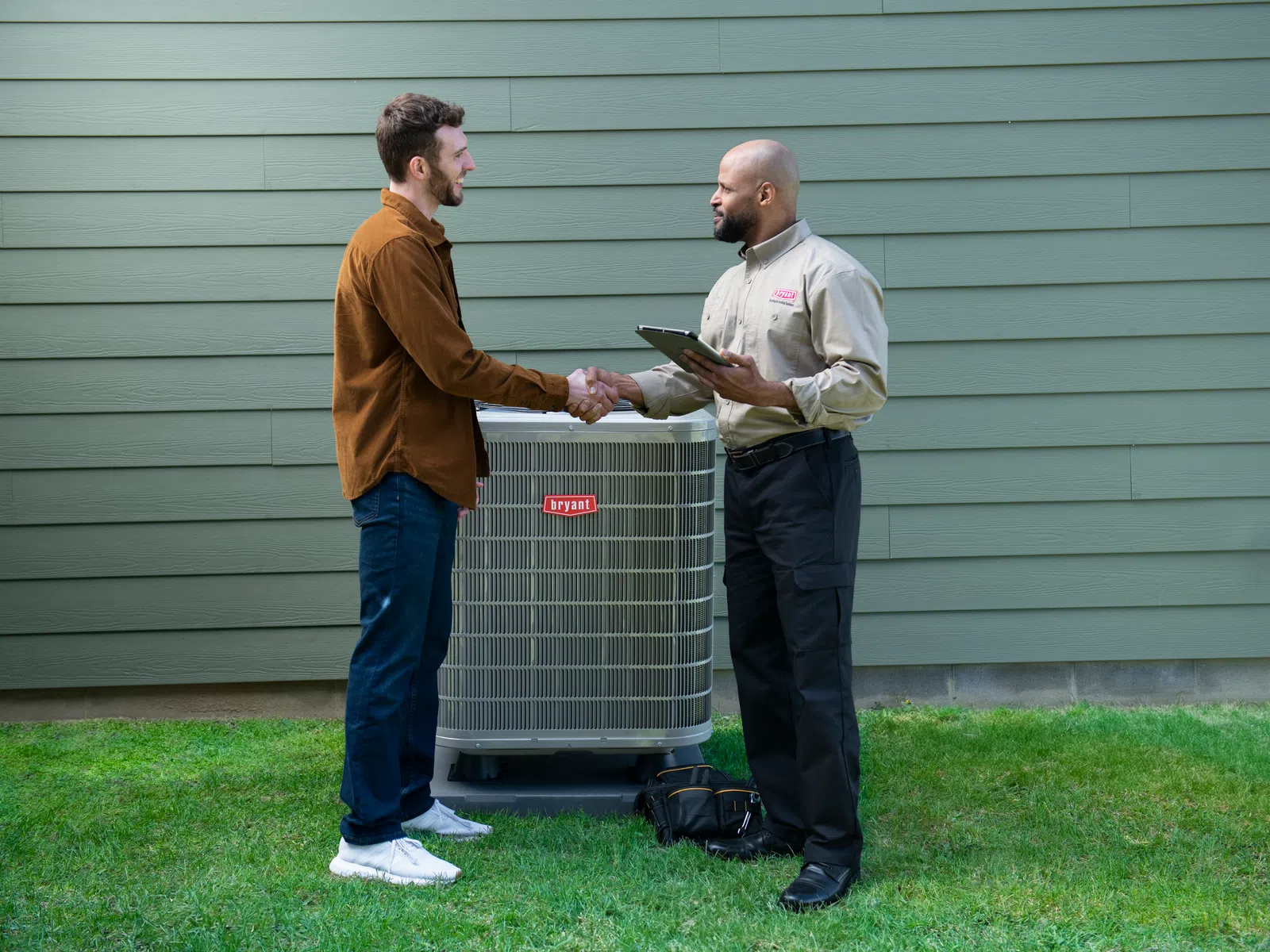 Technician and homeowner shaking hands near new Bryant air conditioning unit outside green house.
