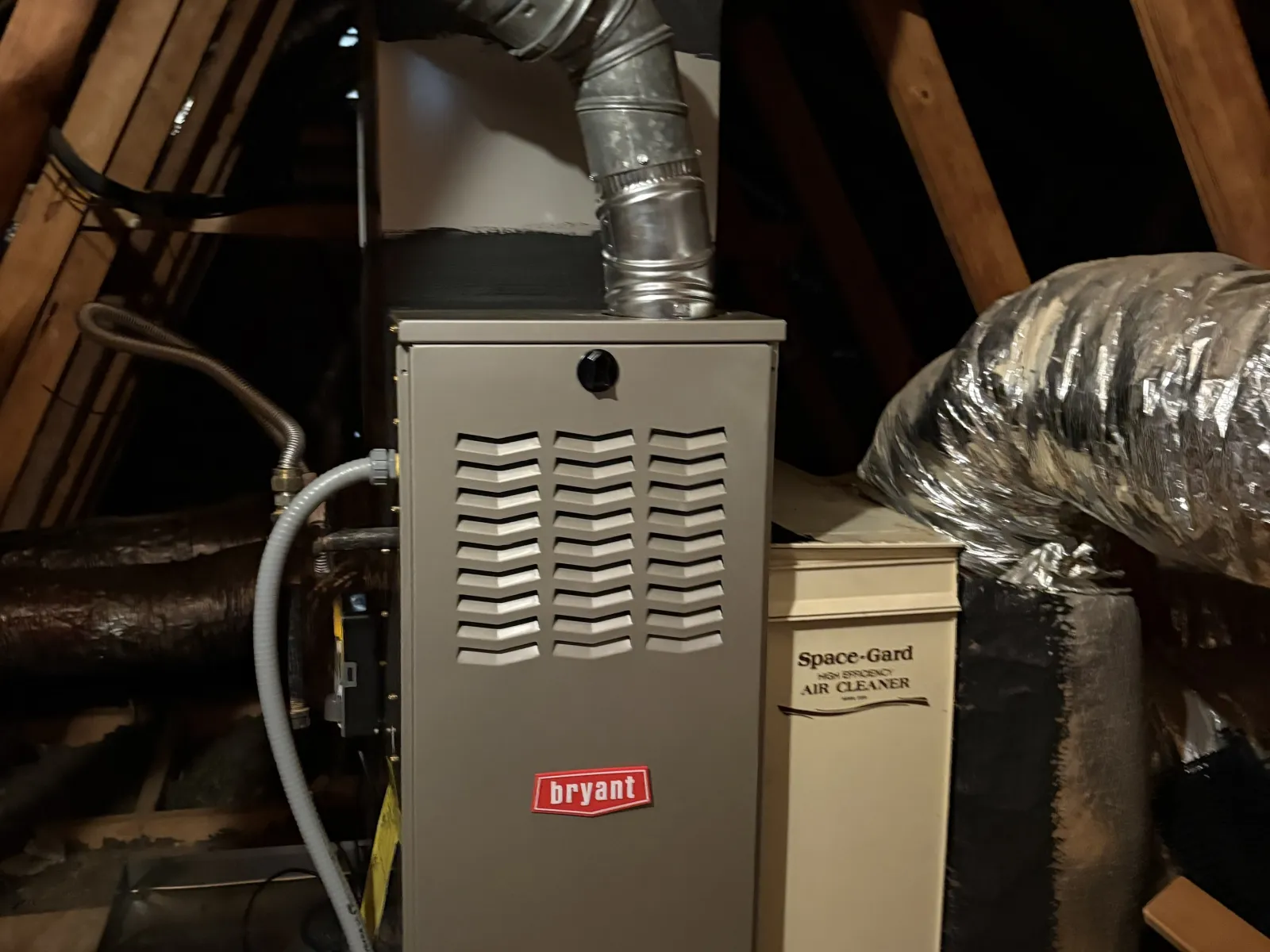 Bryant furnace and Space-Gard air cleaner installed in a wooden attic with ductwork and insulation.