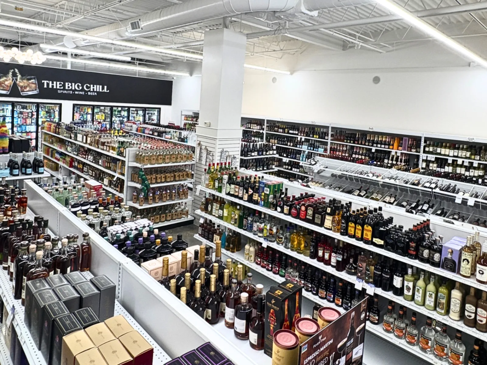Spacious liquor store interior with aisles of wine, spirits, and beer under bright white lighting.