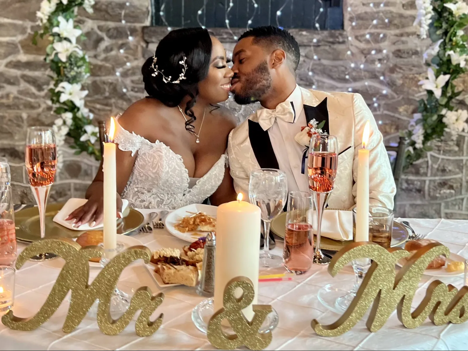 a bride and groom sitting at a table with food and drinks