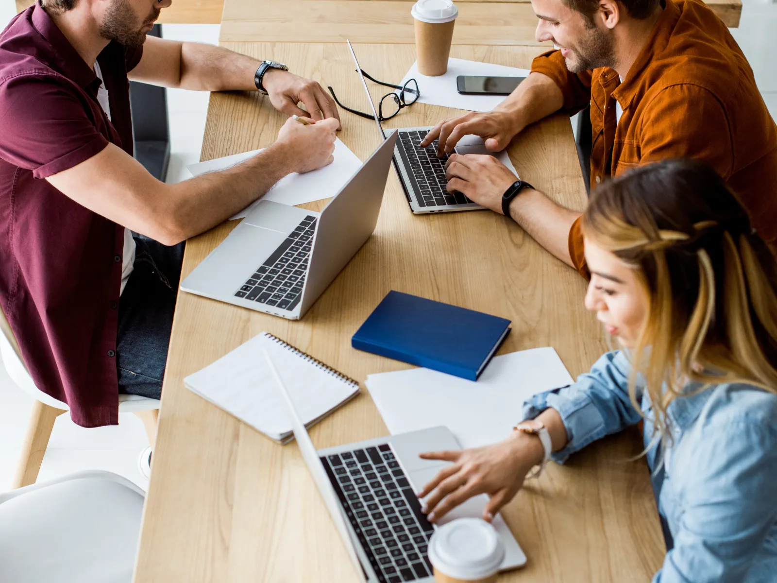 a group of people sitting around a table working on laptops