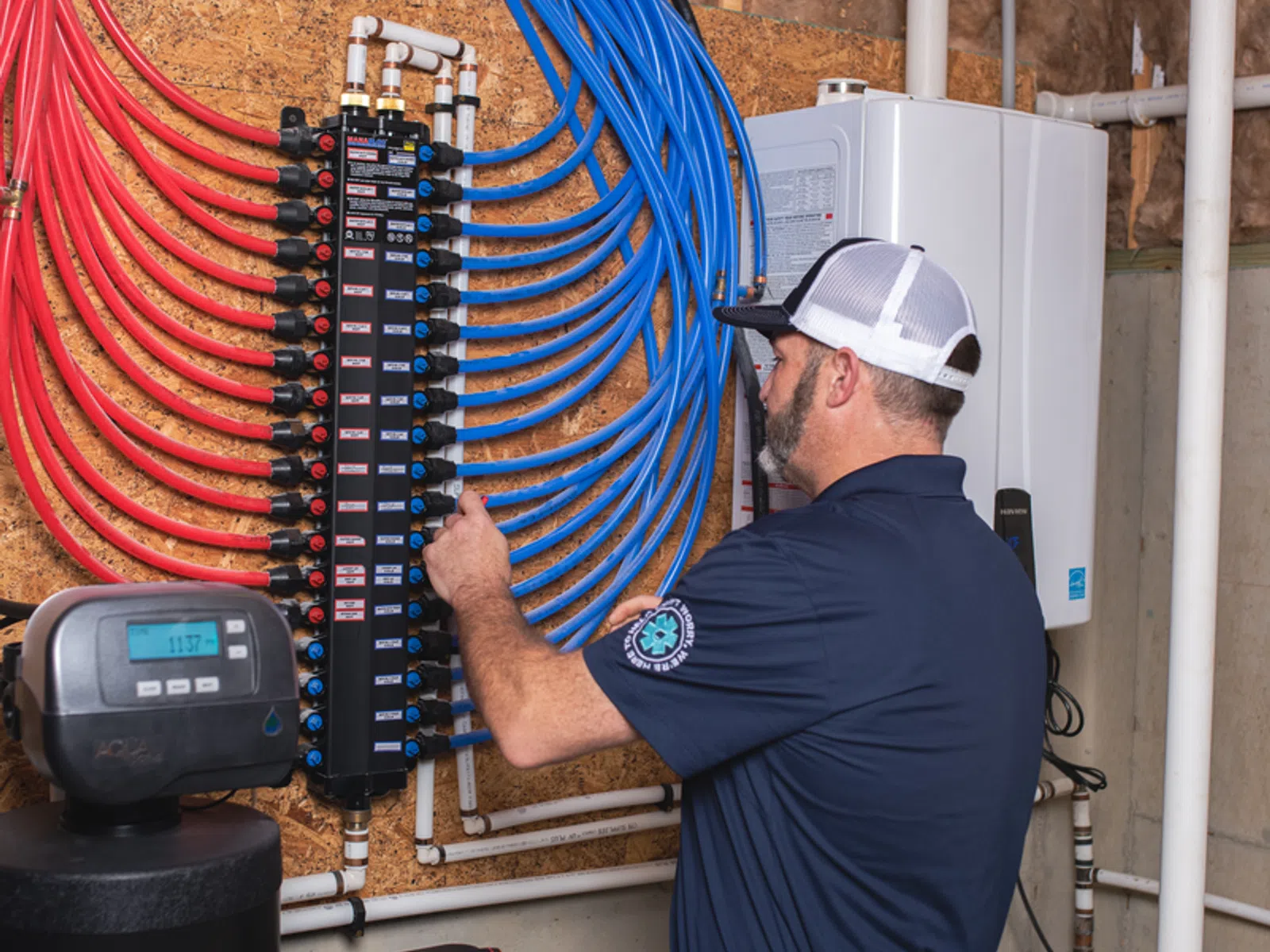 Technician inspecting organized red and blue PEX plumbing pipes and valves in a residential utility room.