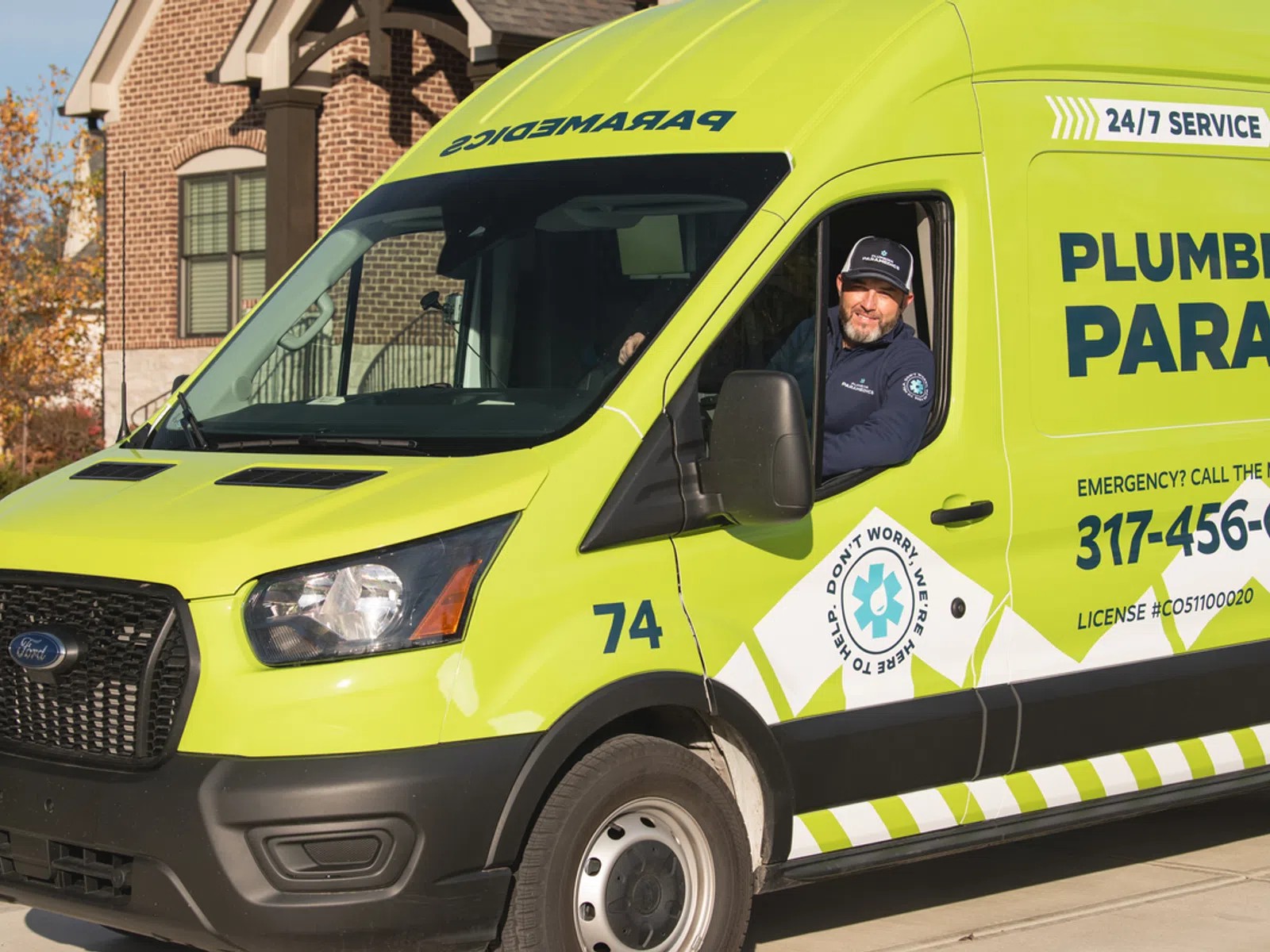 Bright green Plumbing Paramedics service van with driver smiling inside, parked in a residential driveway.