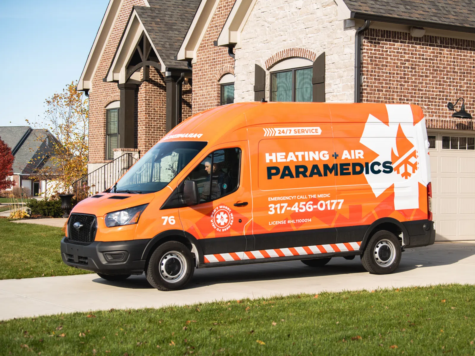 Orange Heating + Air Paramedics service van parked in front of a suburban brick house on a sunny day