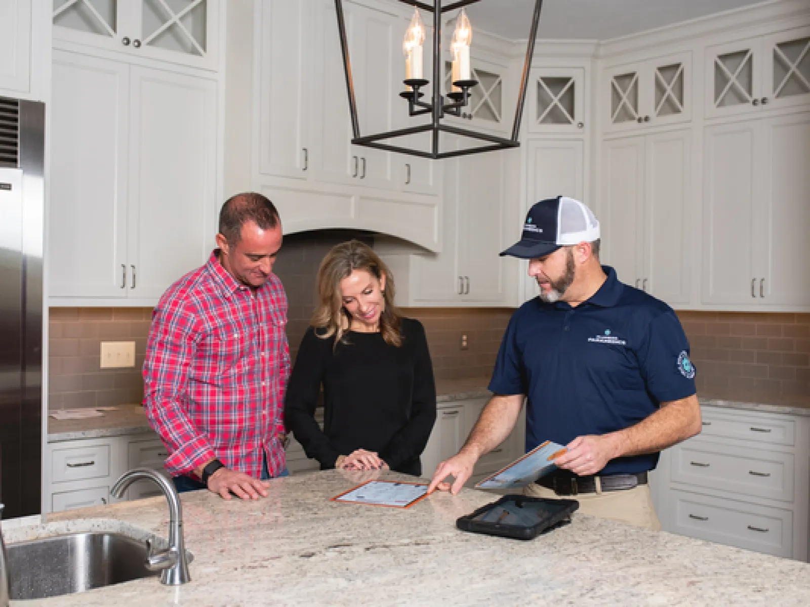 a plumber and homeowners standing inside of a kitchen discussing financing