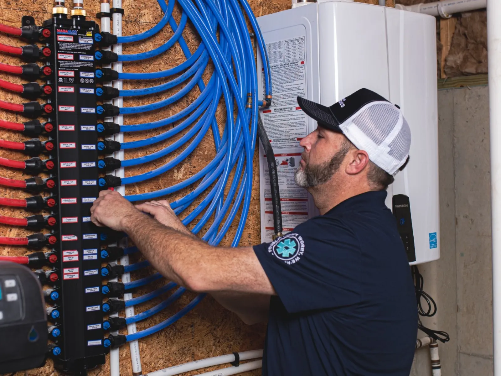 Technician adjusting water heating system with organized blue and red piping in a utility room.