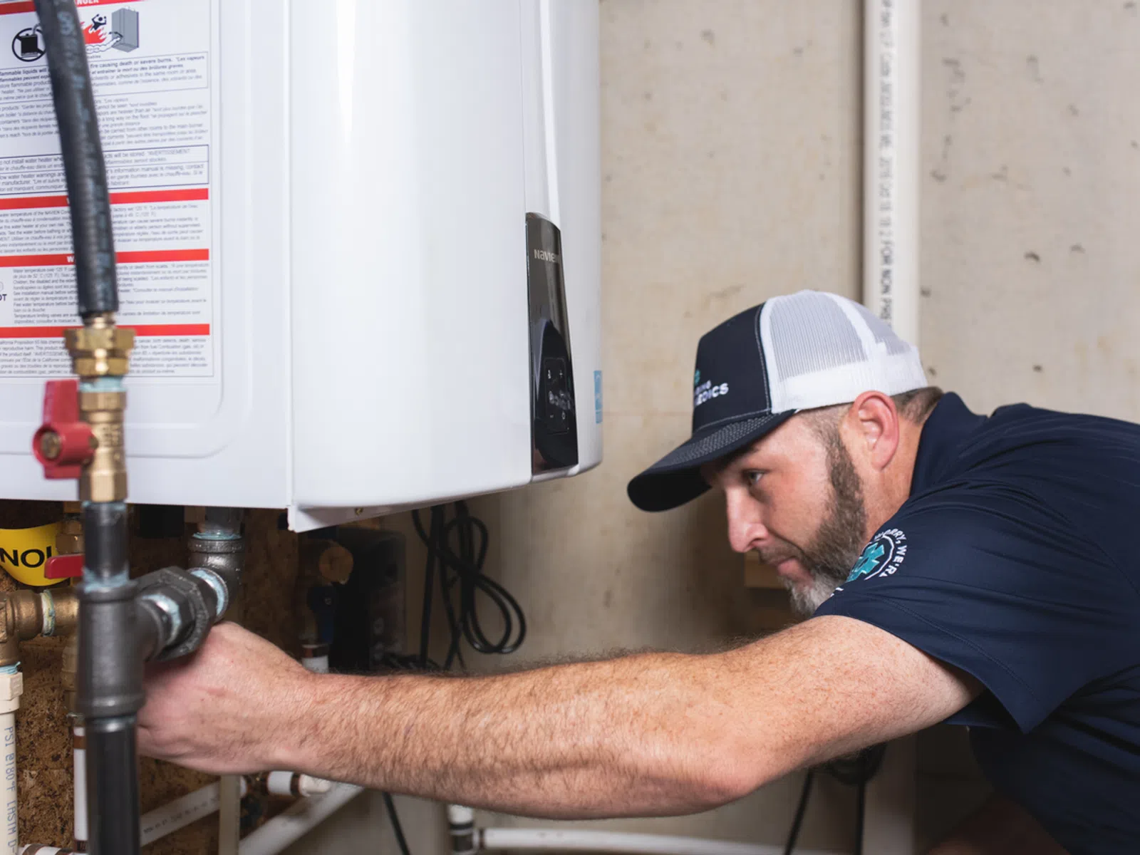 Technician inspecting and adjusting a residential water heater with tools in a utility room.