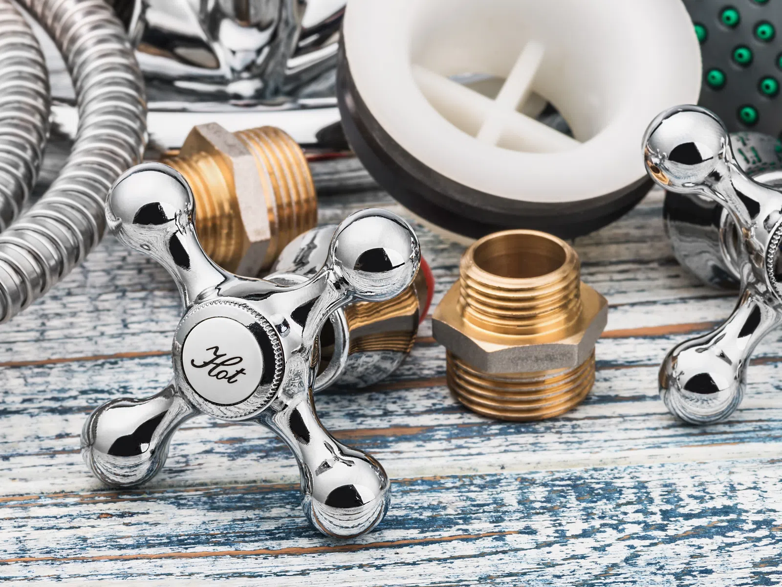 Chrome hot and cold faucet handles with brass fittings and plumbing parts on rustic wooden surface