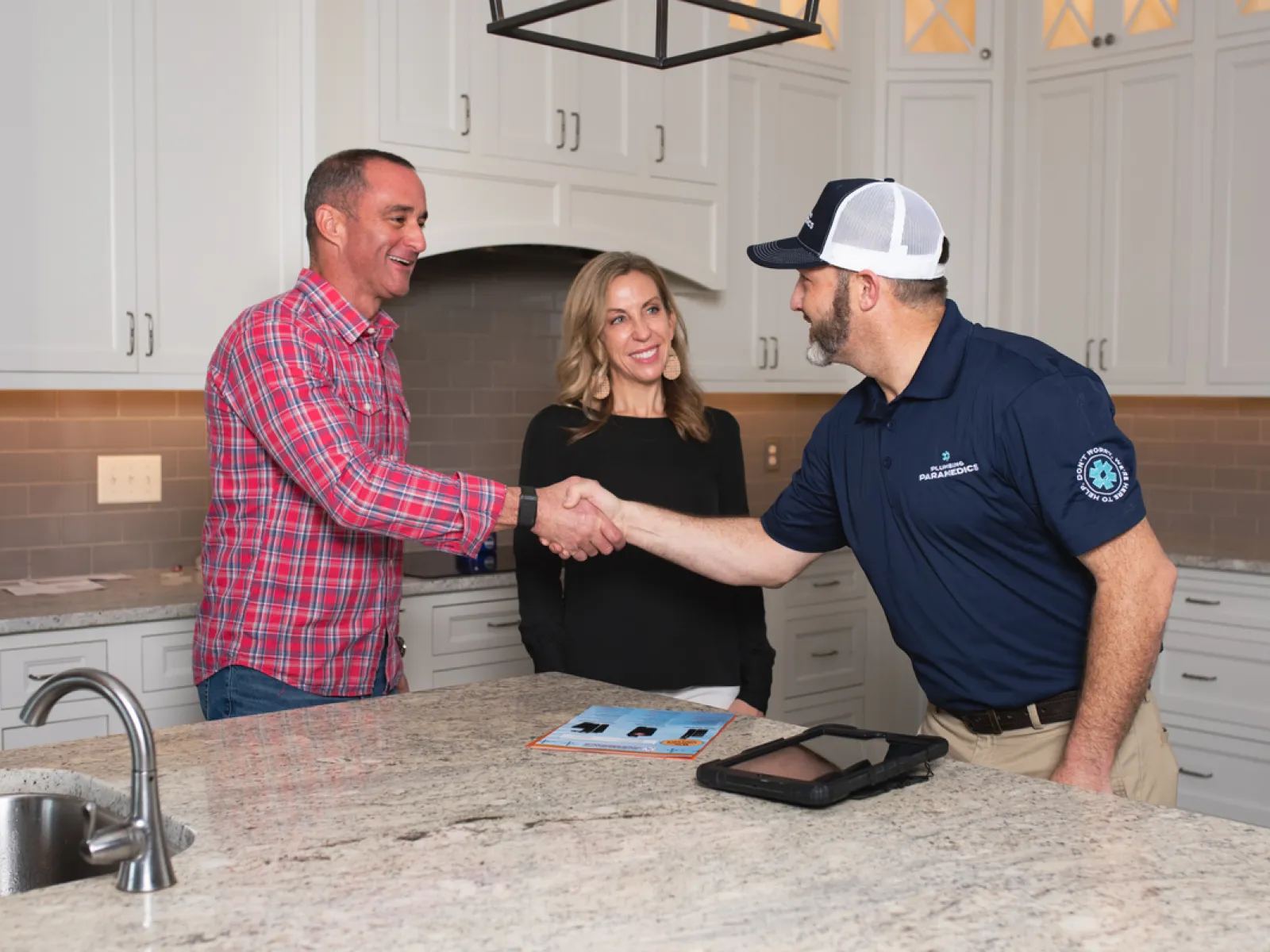 A man shakes hands with a contractor in a modern kitchen while a woman observes, showcasing a professional interaction.