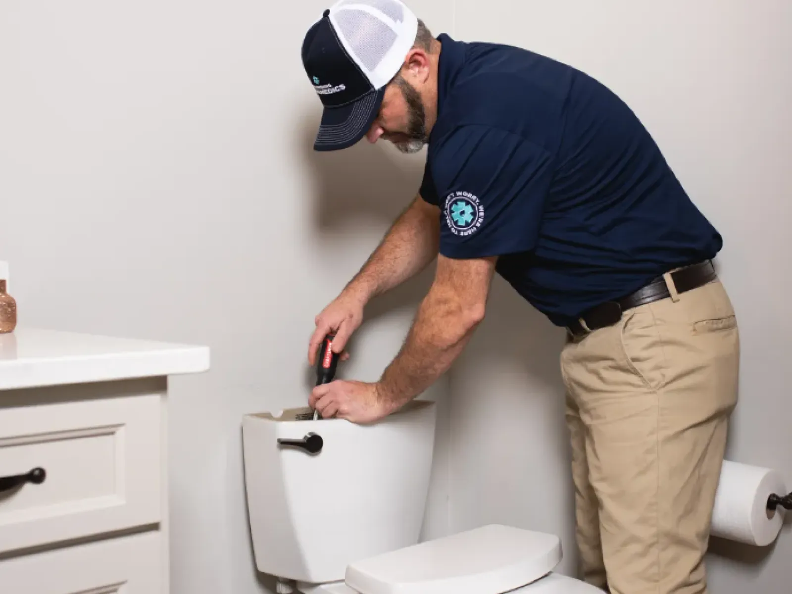 Plumber in uniform fixing the inner mechanism of a toilet tank with a screwdriver in a modern bathroom.