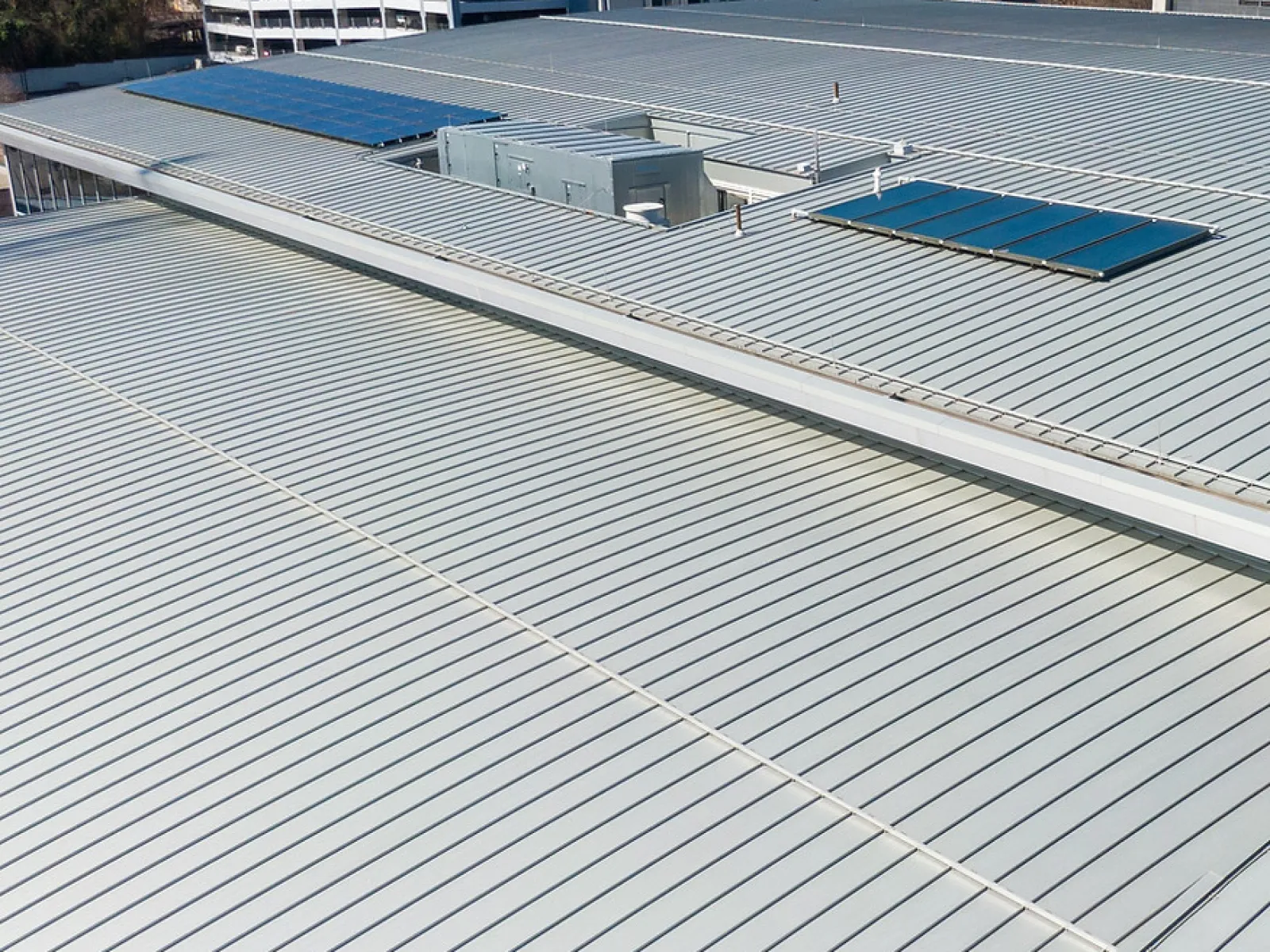 Metal rooftop with solar panels and ventilation units in urban area with office buildings in background