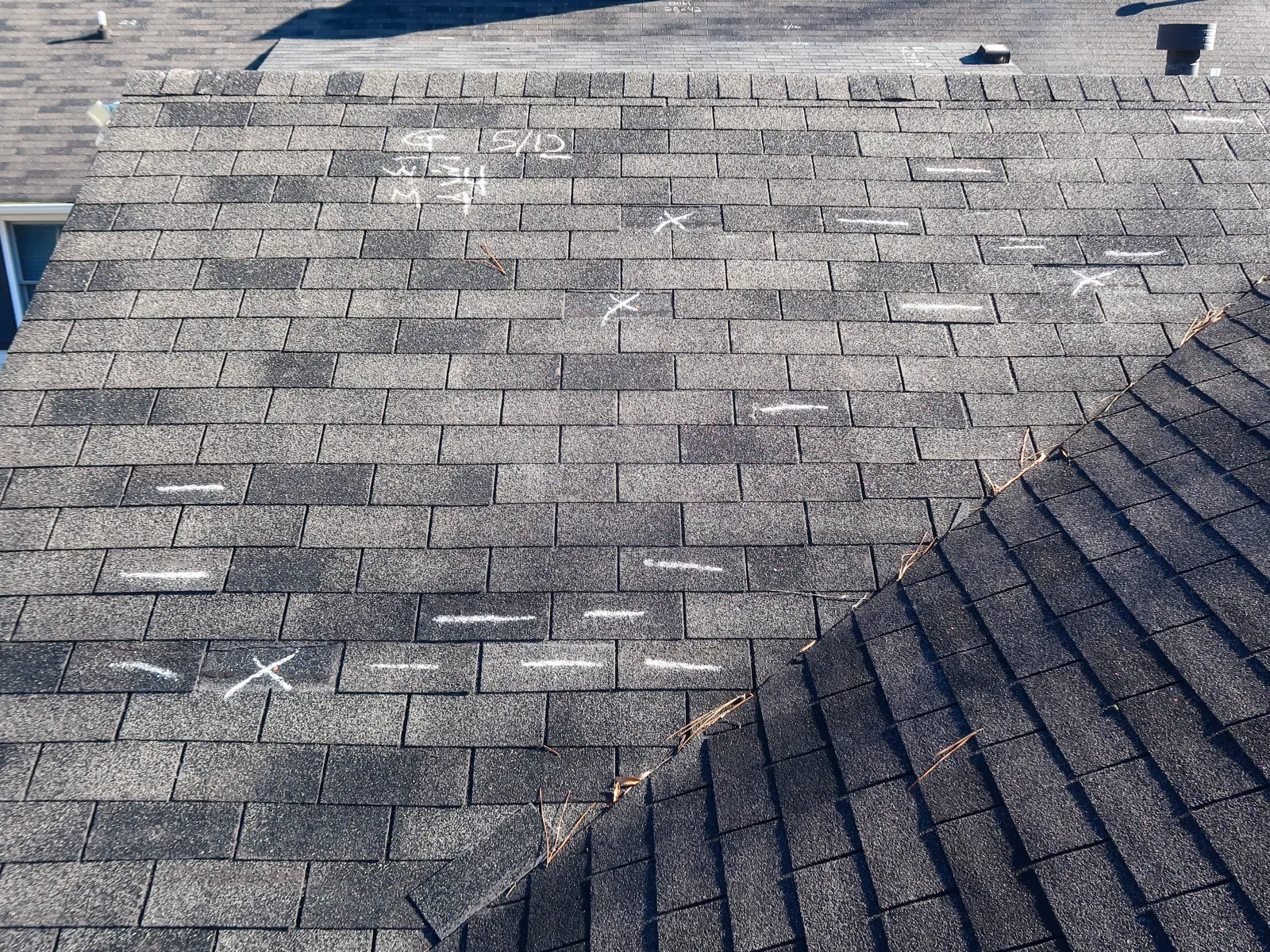 Asphalt shingle roof with white chalk markings indicating damage or repair areas on gray shingles.