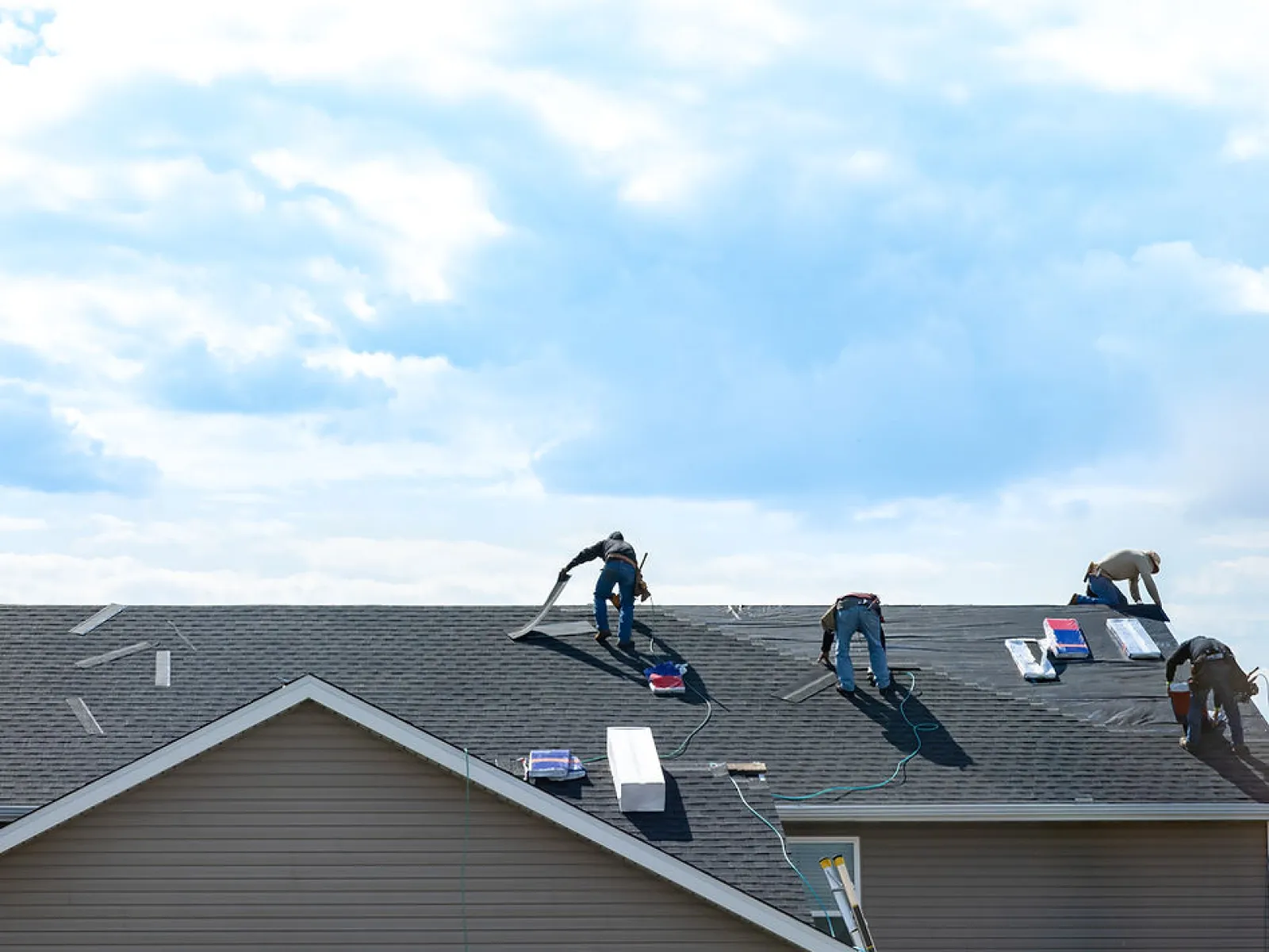 Roofers working on a residential house roof under a partly cloudy sky during daytime.